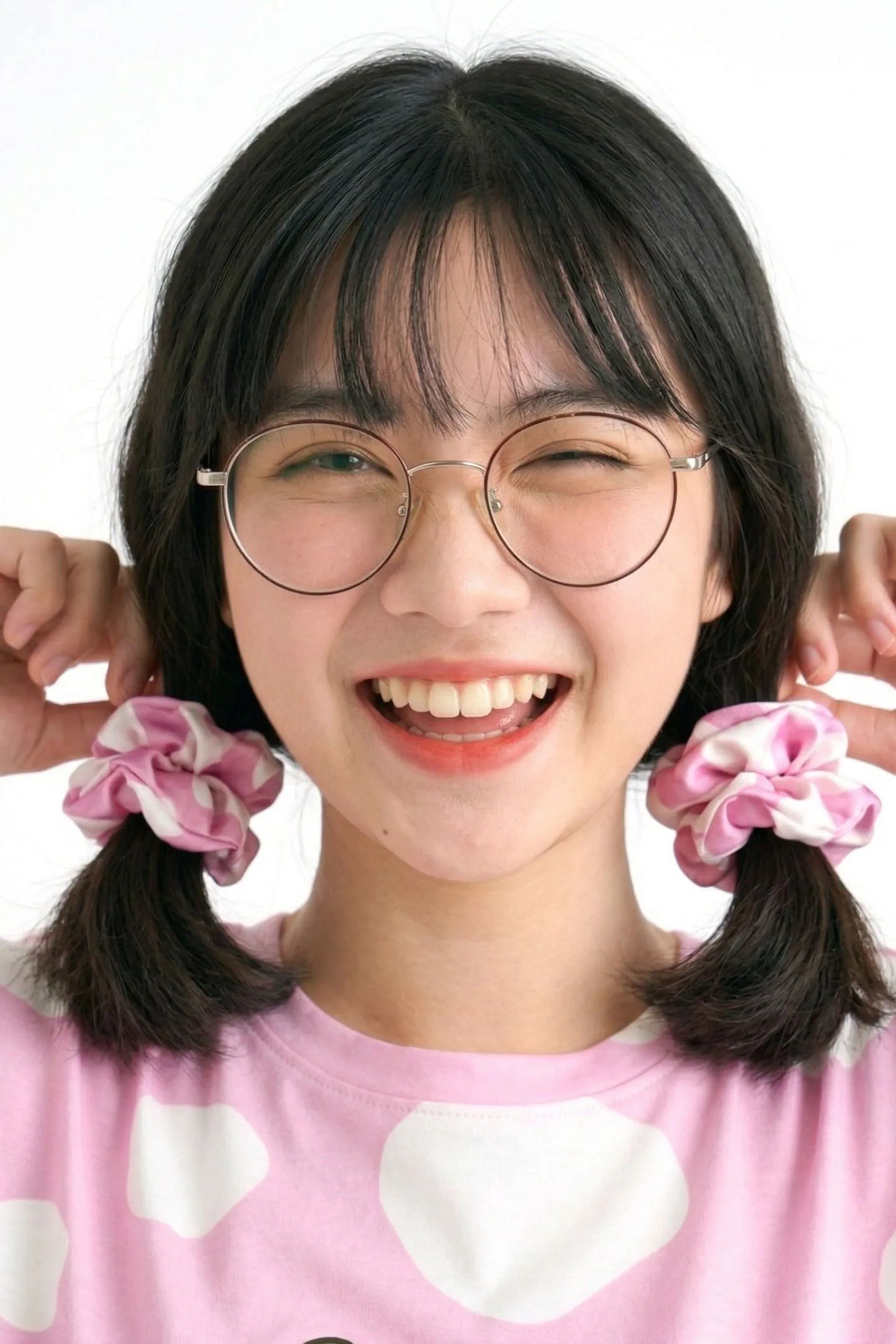 Close-up of woman smiling holding two pink cow print bamboo scrunchies beside her face