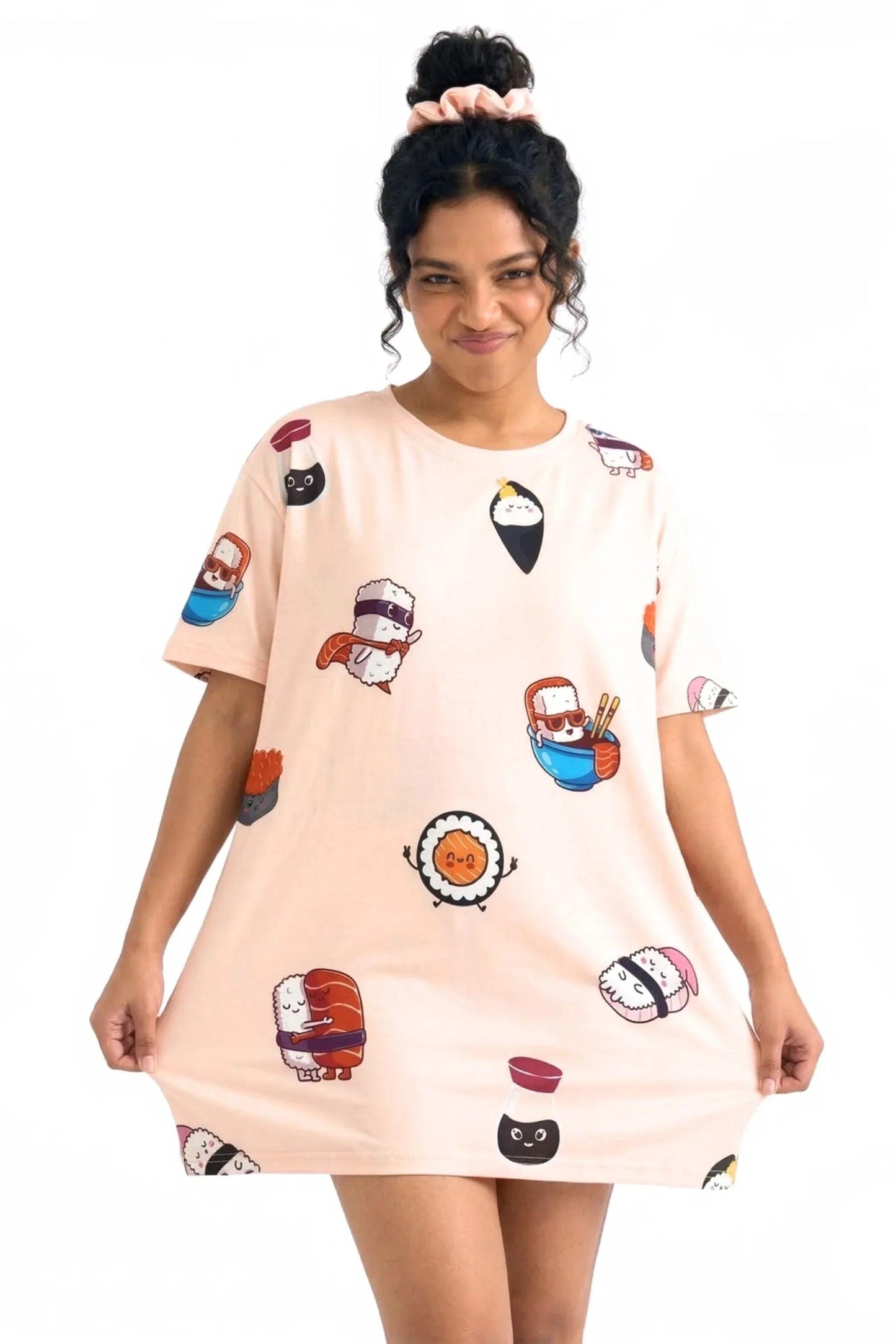 A smiling woman smiling and stretching the hem of a light pink MySleepTee™ Soy Cozy Petite bamboo sleep dress featuring cute cartoon sushi characters. She is wearing a matching scrunchie.