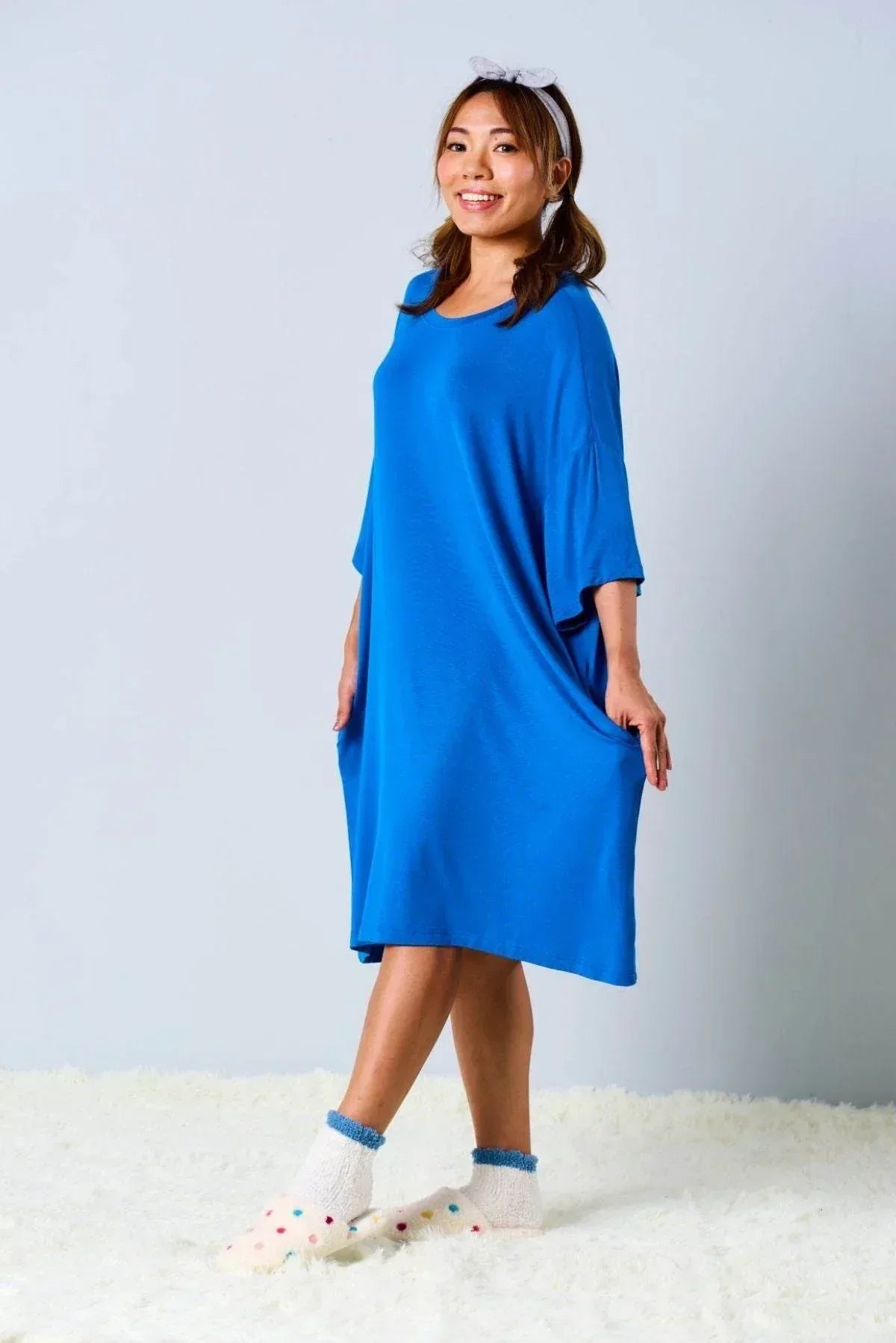 Woman wearing a blue sleepwear standing on a white surface with a light gray background