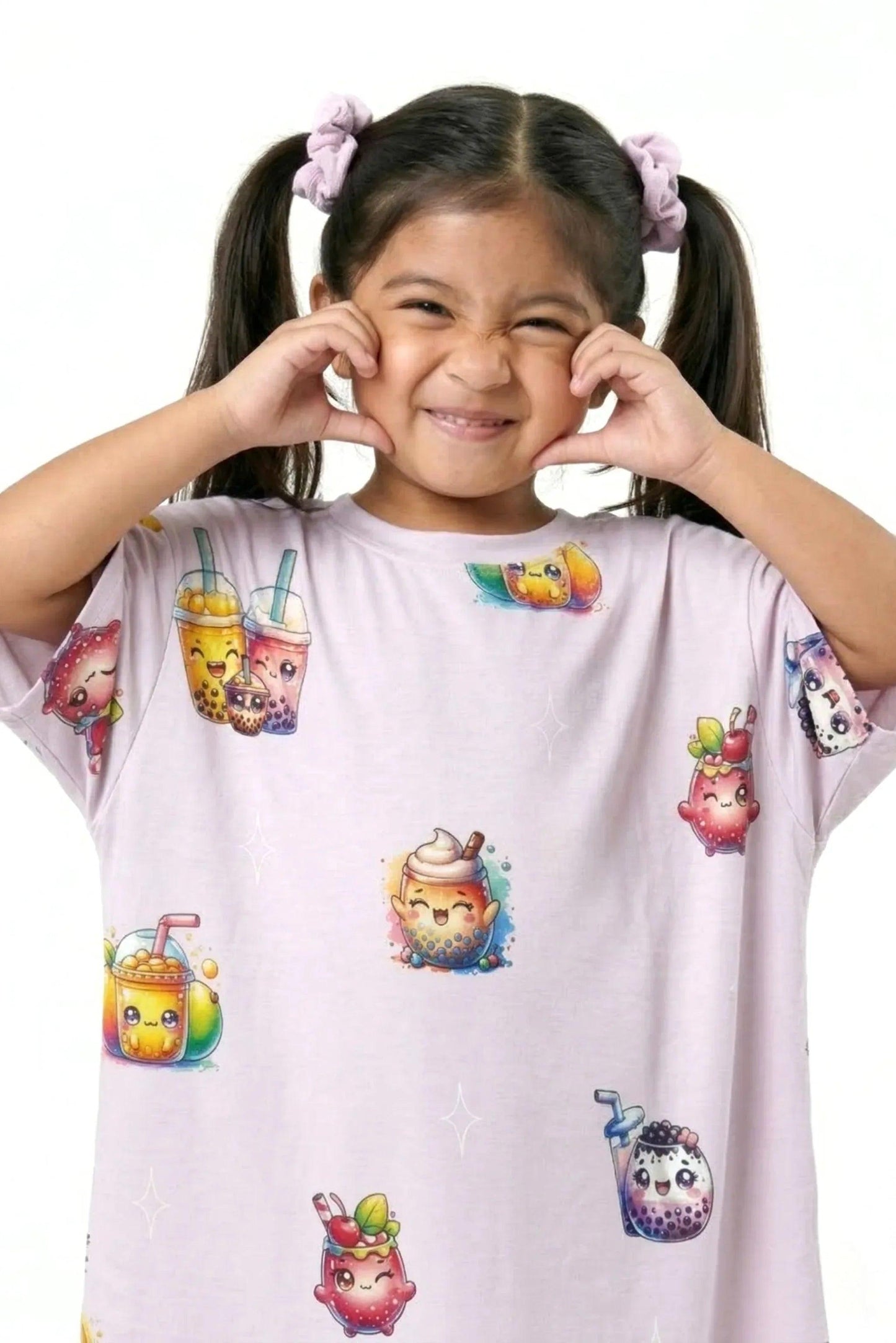 A close-up of a smiling little girl with pigtails playfully squishing her cheeks. She is wearing the light purple MySleepTee™ The Bubble Tee | Kids sleep dress, featuring cute and colorful cartoon bubble tea characters.