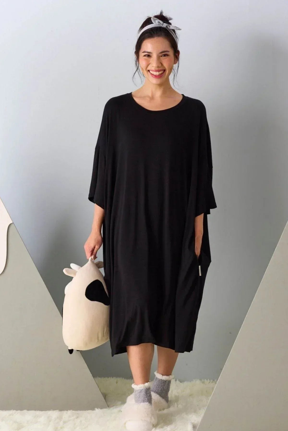 Woman wearing a black loungewear holding a plush toy against a neutral background