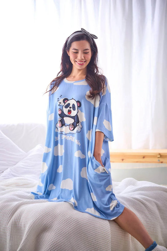 Woman wearing a blue bamboo sleep tee by mysleeptee with a panda design, sitting on a bed.