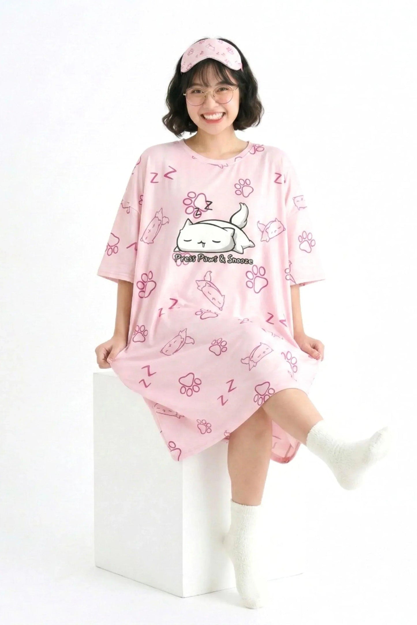 MySleepTee pink oversized bamboo nightshirt for women, shown in a full-length view on a sitting model with white socks and a matching sleep mask.