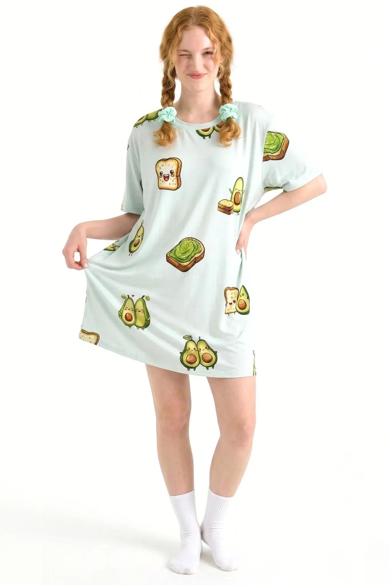 Red-haired model winking and holding the hem of the Avo-Good Night Petite sleep tee, made from cooling bamboo sleepwear fabric with an avocado print.