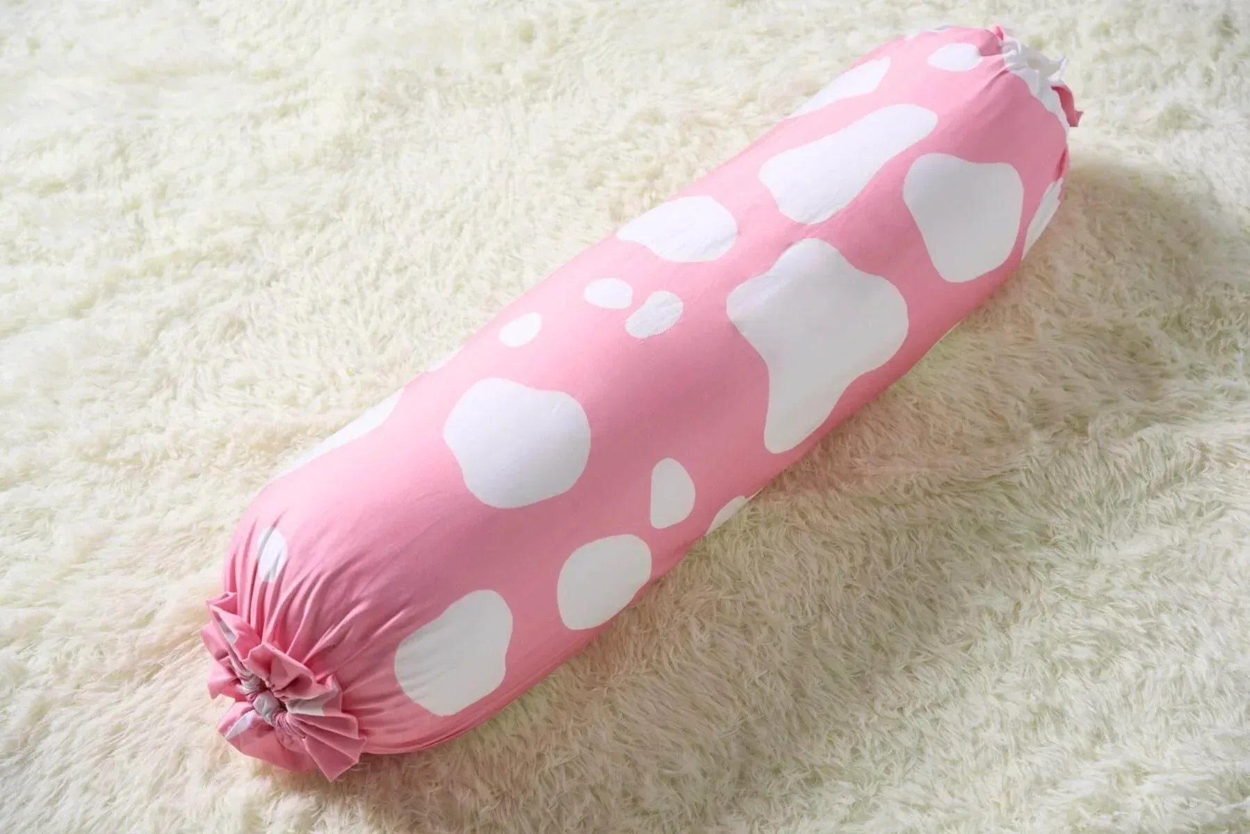 Pink bolster with white cow patterns on a light beige surface