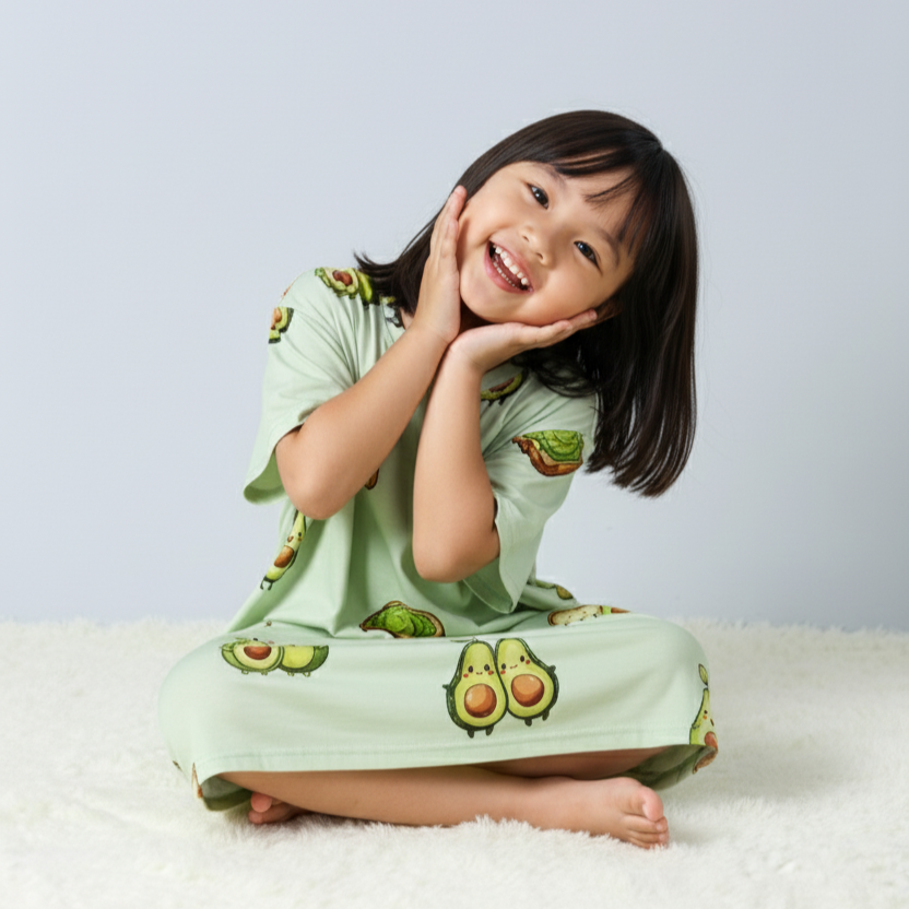 Child wearing a green oversized sleep tee from MySleepTee with avocado prints on a white background