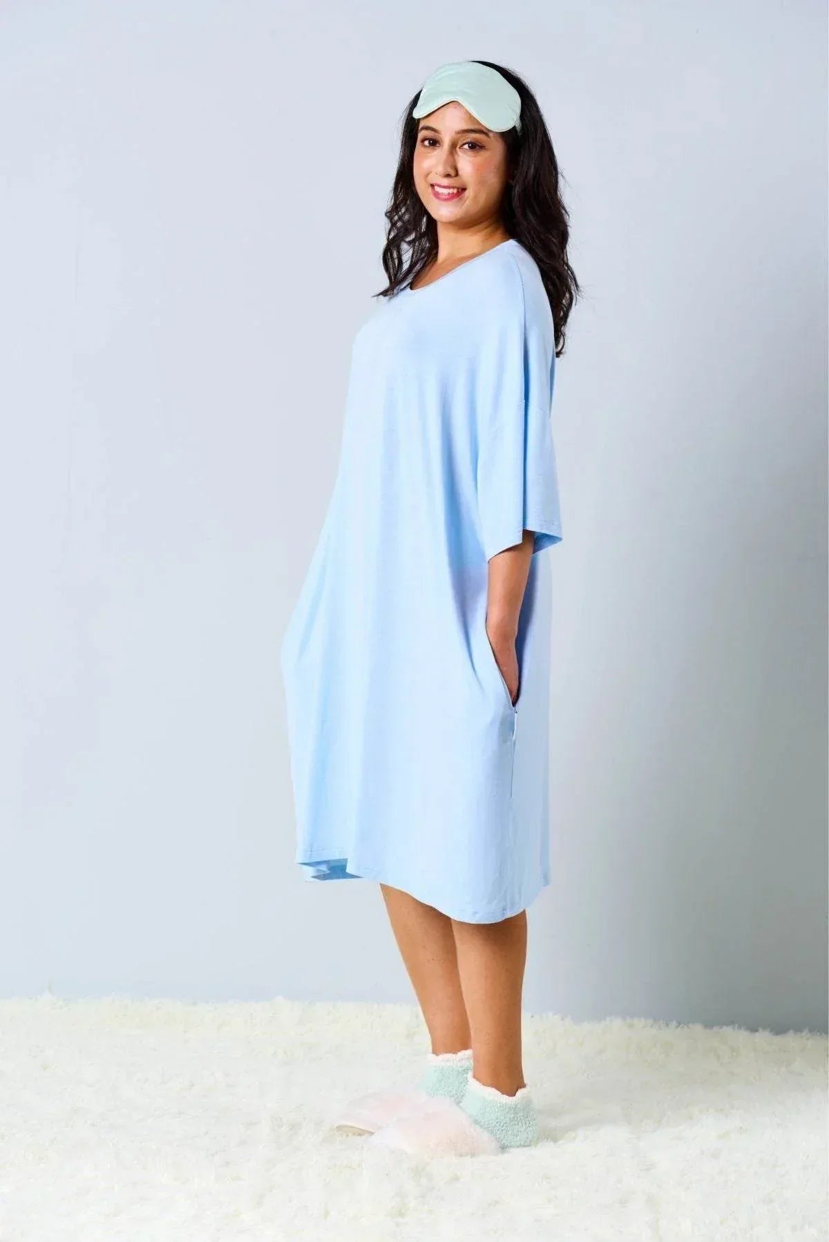 Woman wearing a light blue sleep tee by MySleepTee and a blue sleep mask on a plain background