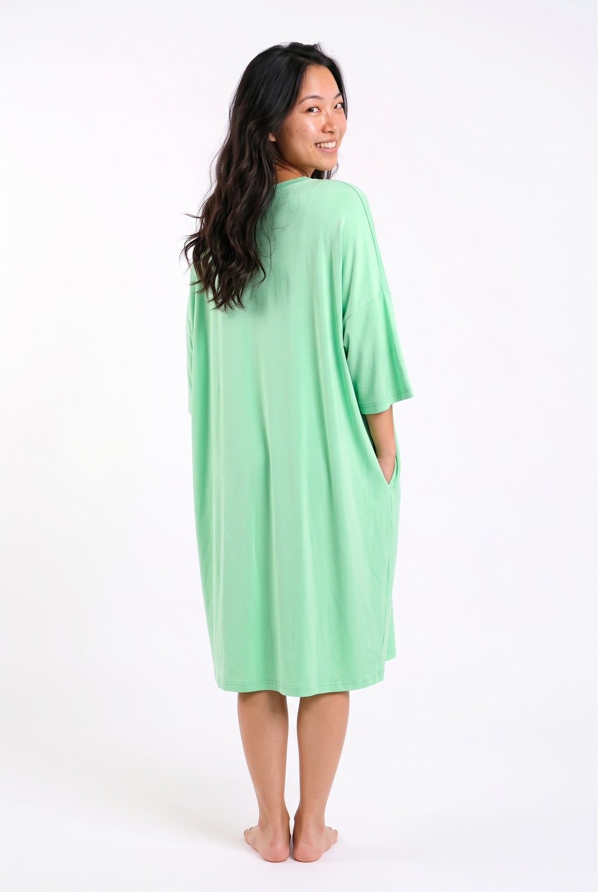Mint green bamboo oversized sleep tee, back view showing the knee-length hem, dropped shoulders and relaxed drape, model smiling over her shoulder
