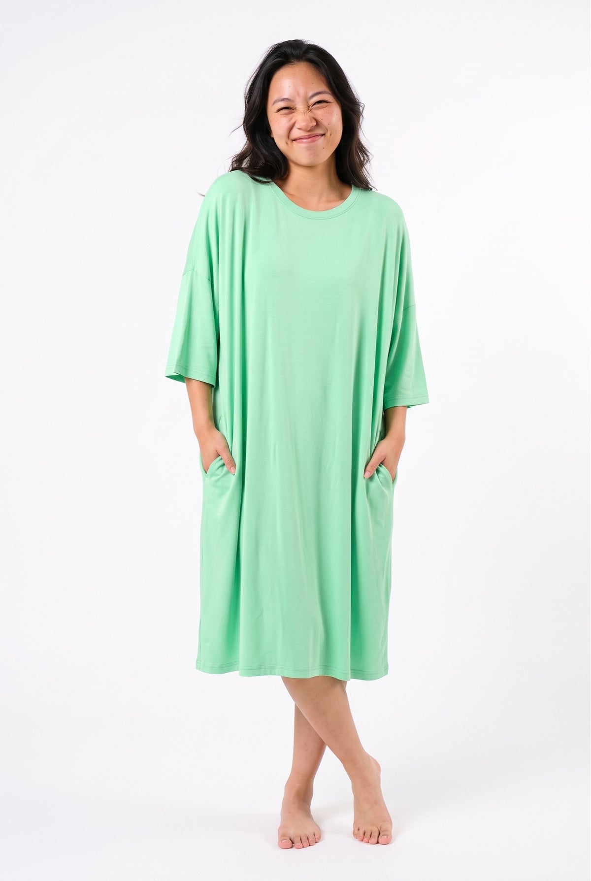 Mint green bamboo oversized sleep tee, front view with both hands in the hidden side pockets, showing the knee-length hem and wide dropped sleeves