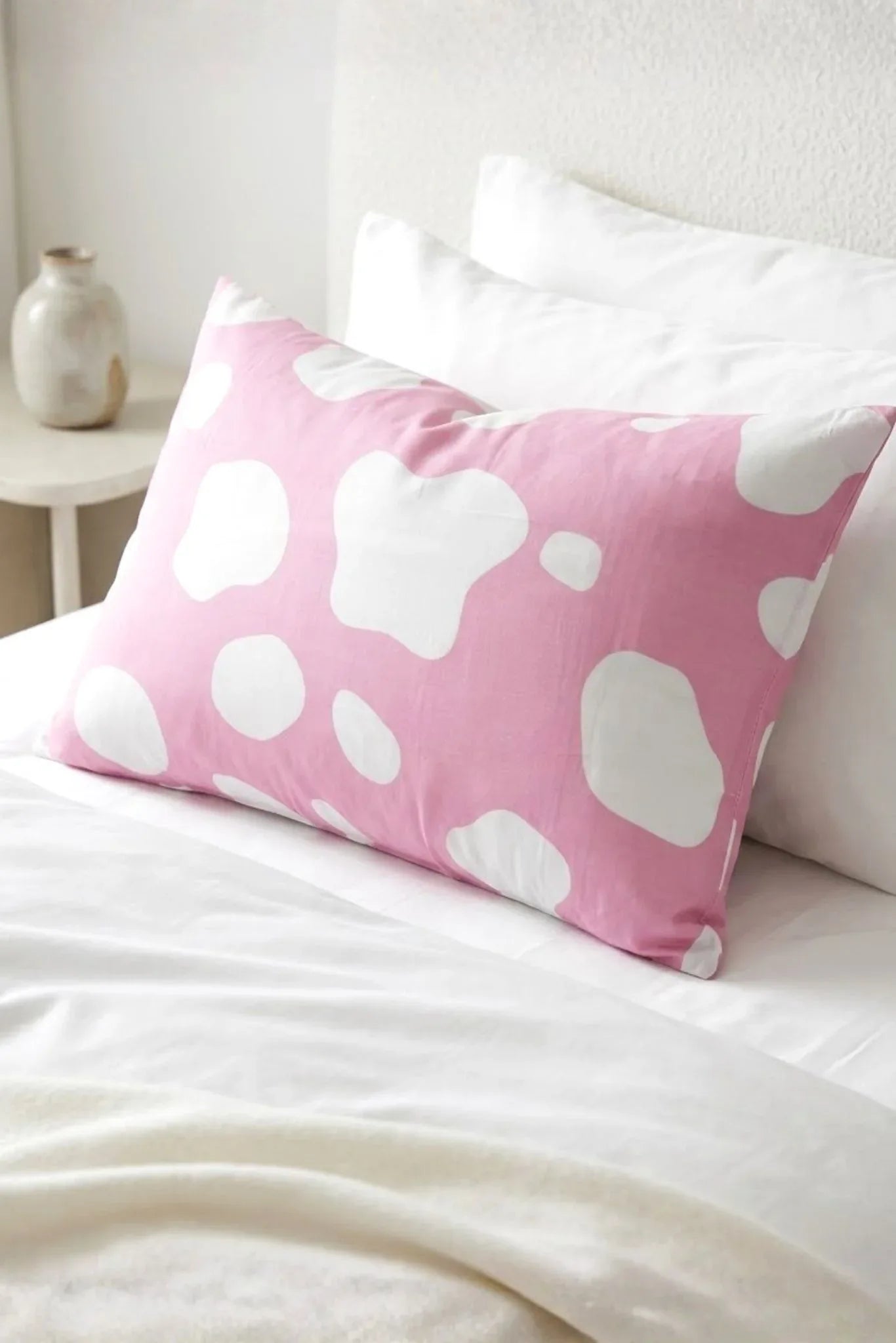 Pink cow print bamboo pillow case styled on white bed sheets in cozy bedroom setting