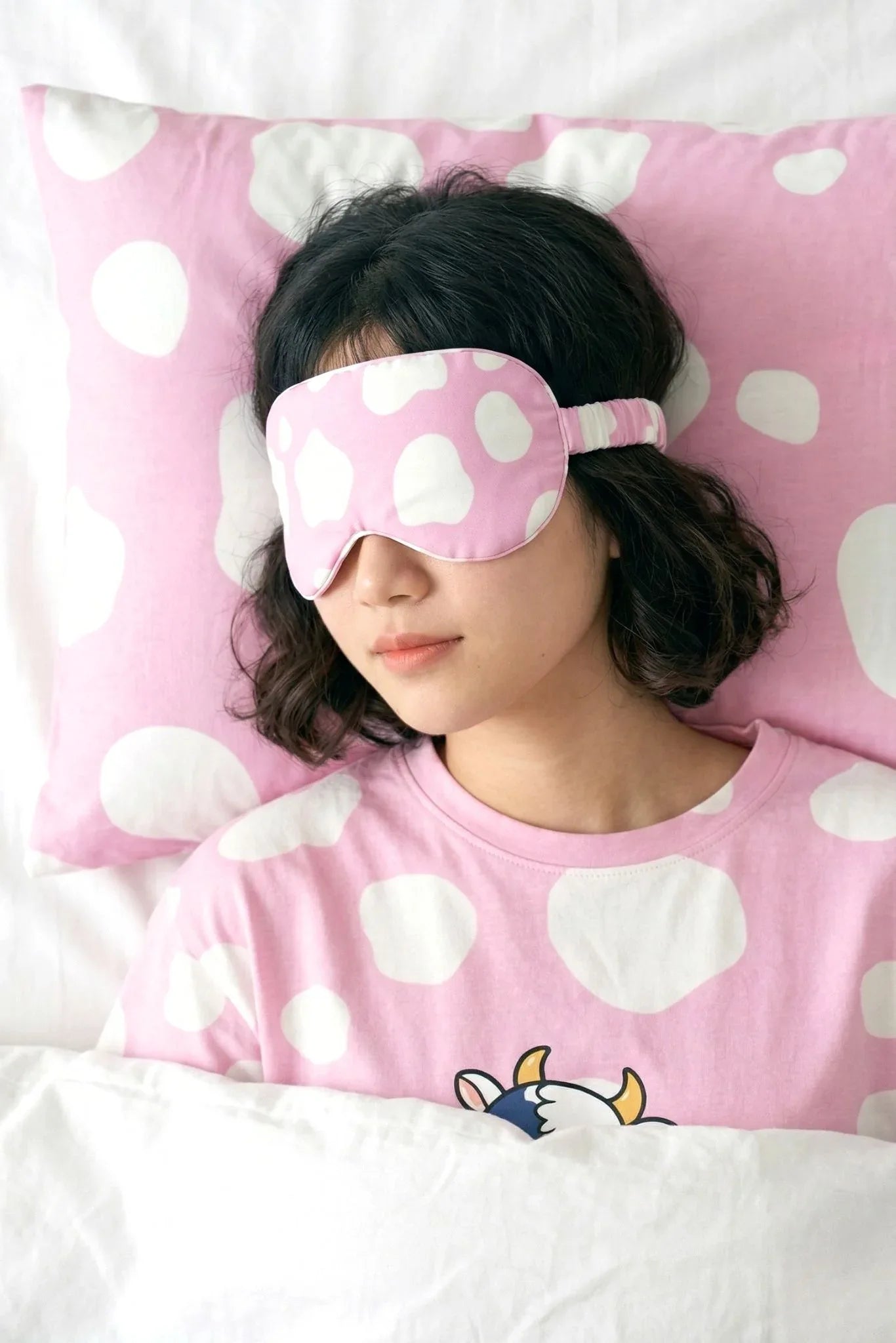 Woman sleeping on pink cow print bamboo pillow case wearing matching sleep mask and sleep tee