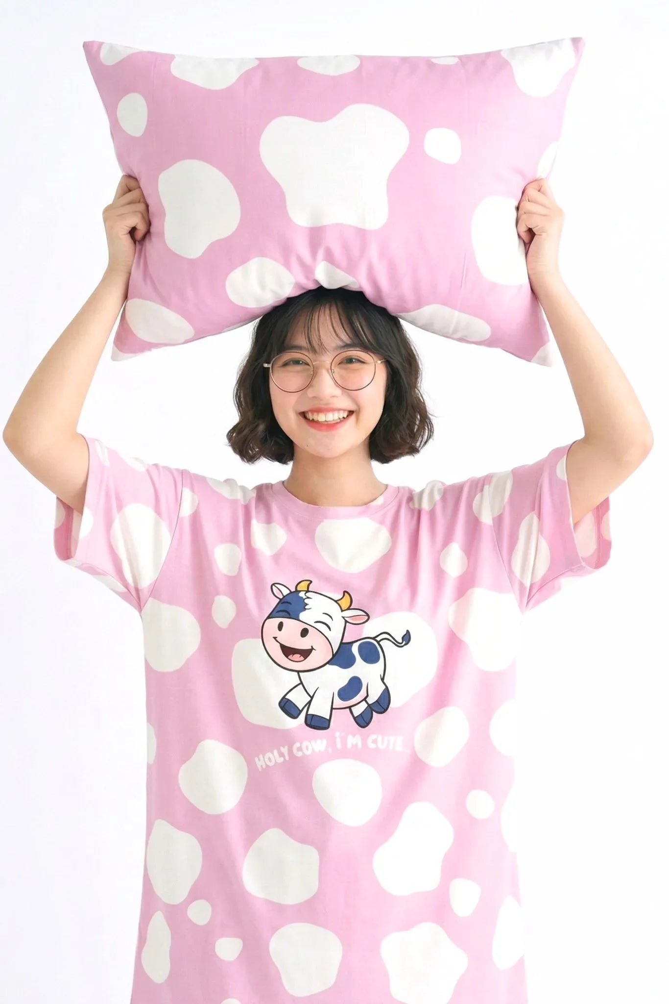 Woman holding pink cow print bamboo pillow case above head wearing matching Moo-nlight bamboo sleep tee