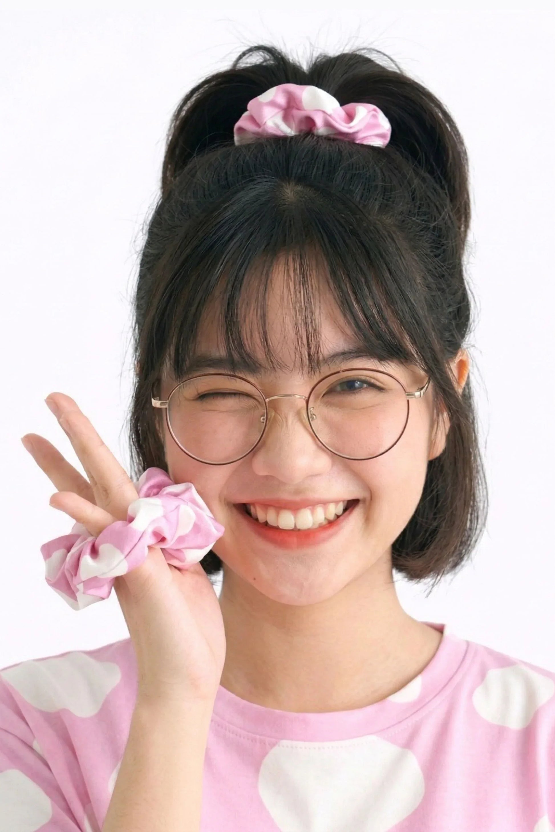 Woman styling bamboo scrunchie in high bun with second scrunchie on wrist showing cow print design