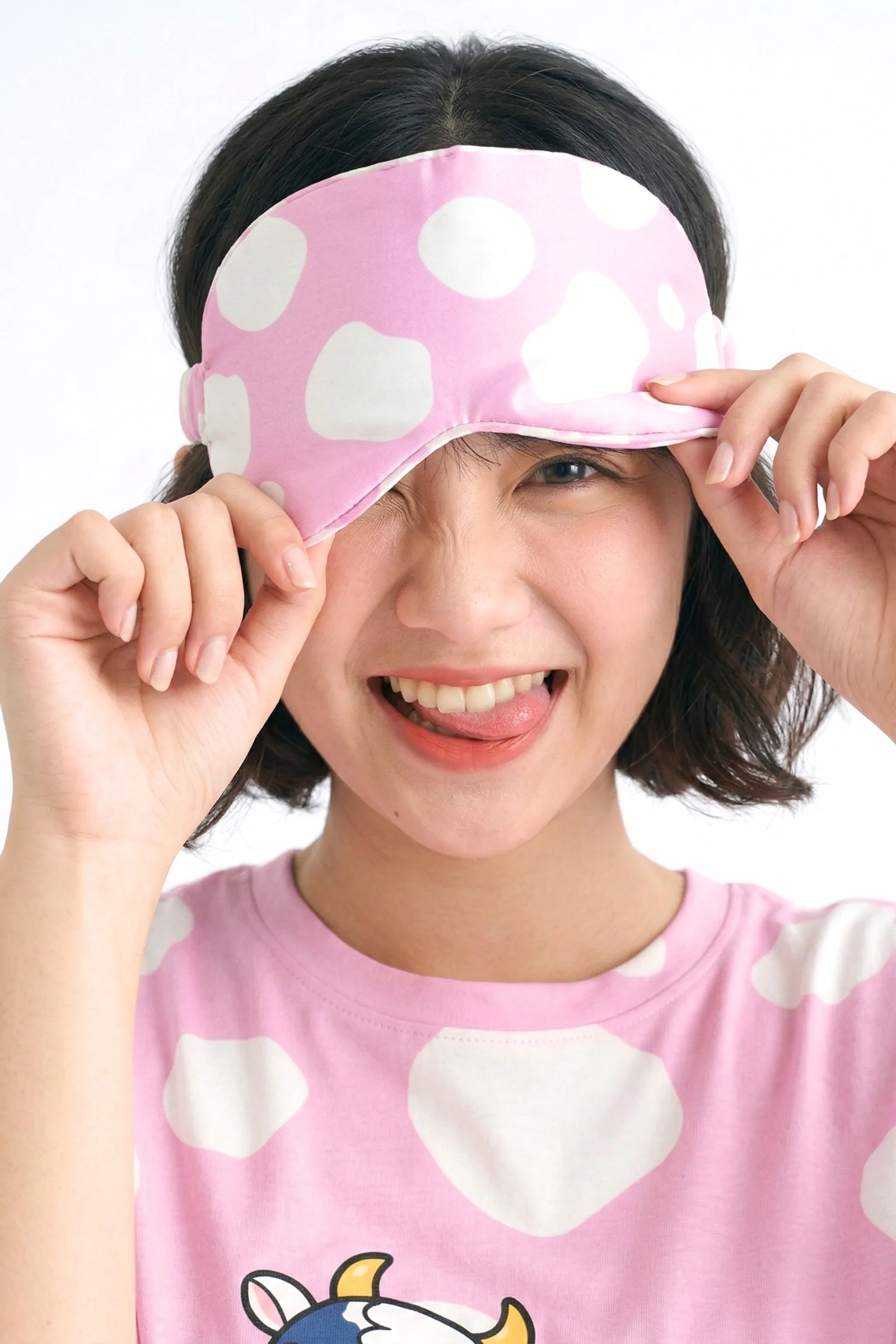 Woman playfully lifting pink cow print bamboo sleep mask showing soft bamboo fabric