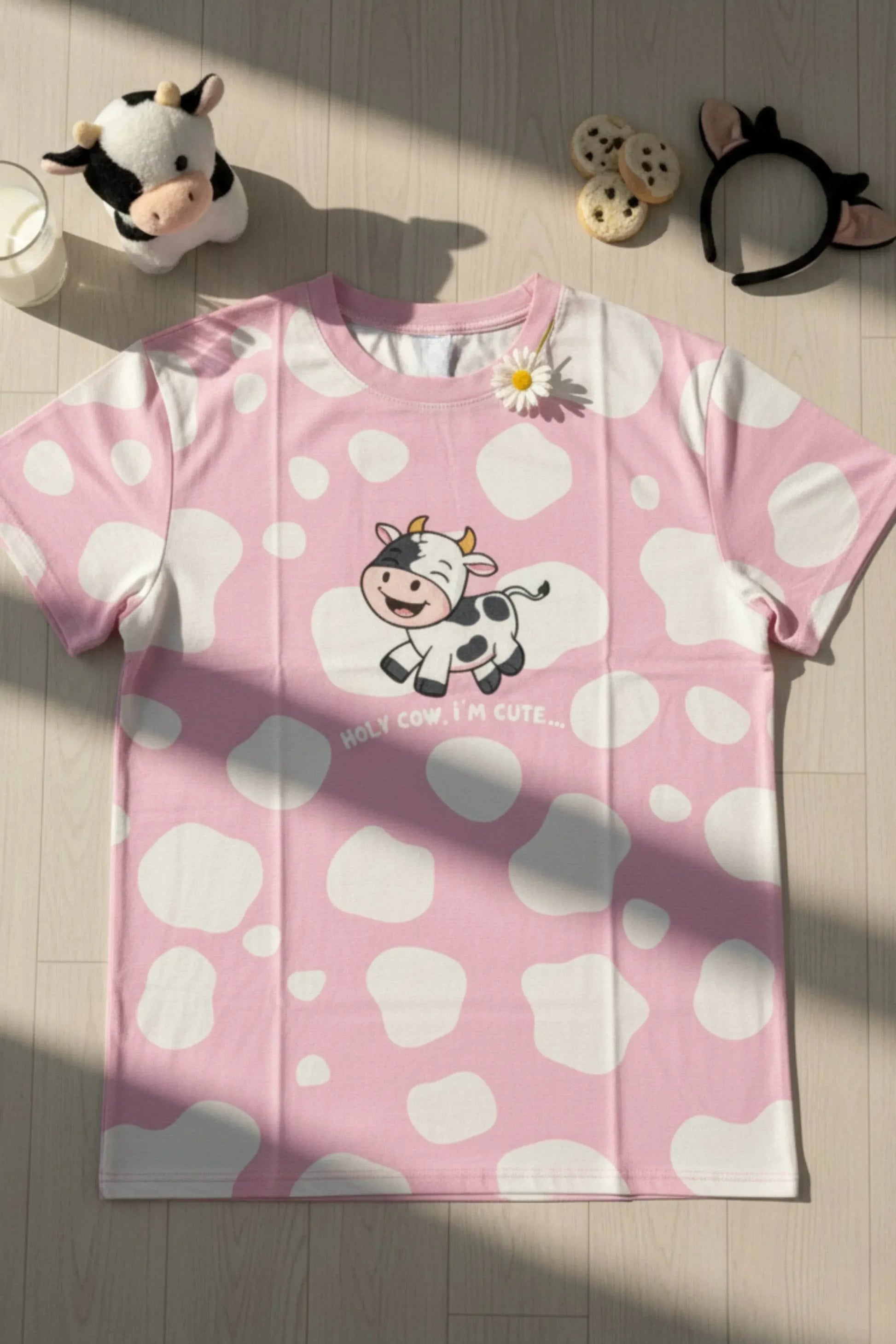 Flat lay shot of a oversized bamboo sleep tee from MySleepTee. Pink Shirt with a cow design on a wooden floor with a plush cow and milk 