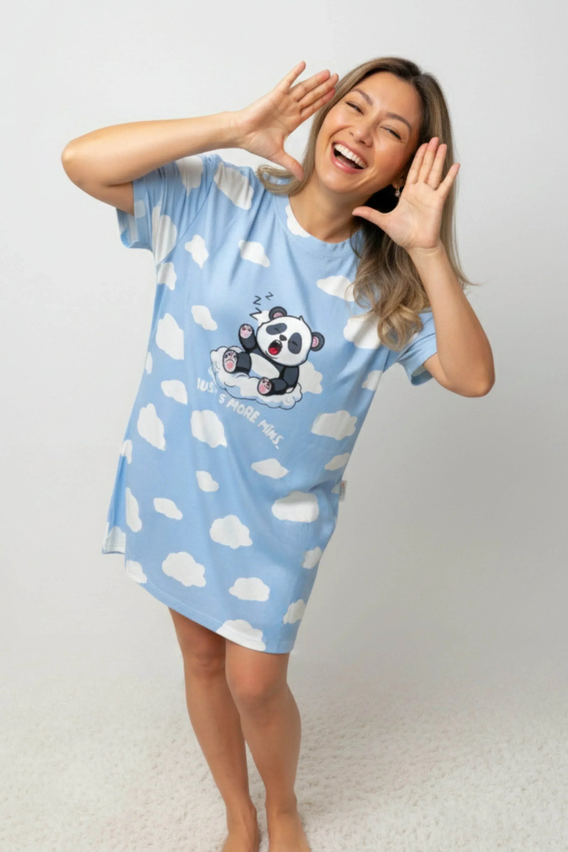 Woman wearing a blue sleep tee from MySleepTee with cloud patterns and a panda design, standing against a plain background.