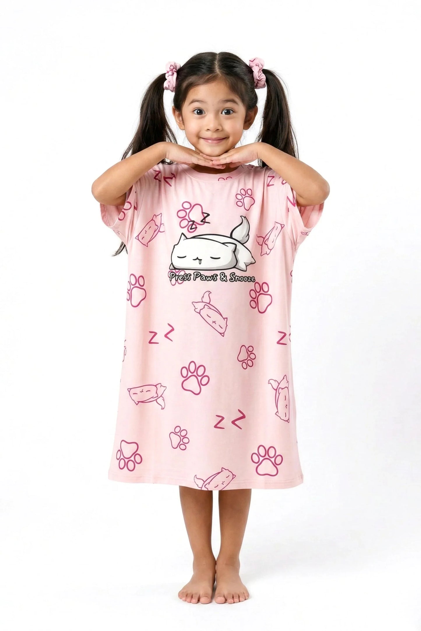 A happy child posing with hands under her chin in a pink MySleepTee bamboo nightshirt with an all-over cat and paw print.