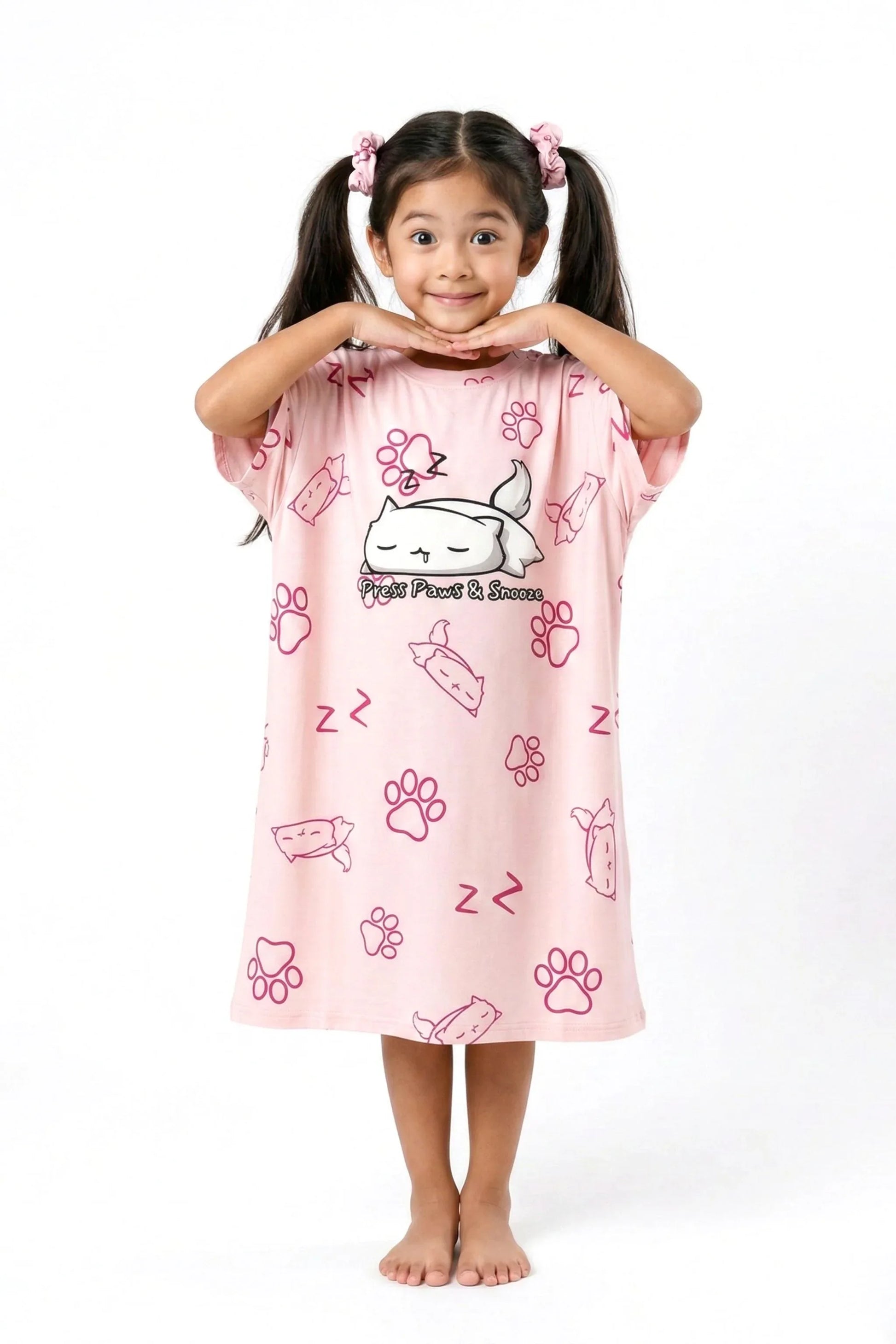 A happy child posing with hands under her chin in a pink MySleepTee bamboo nightshirt with an all-over cat and paw print.