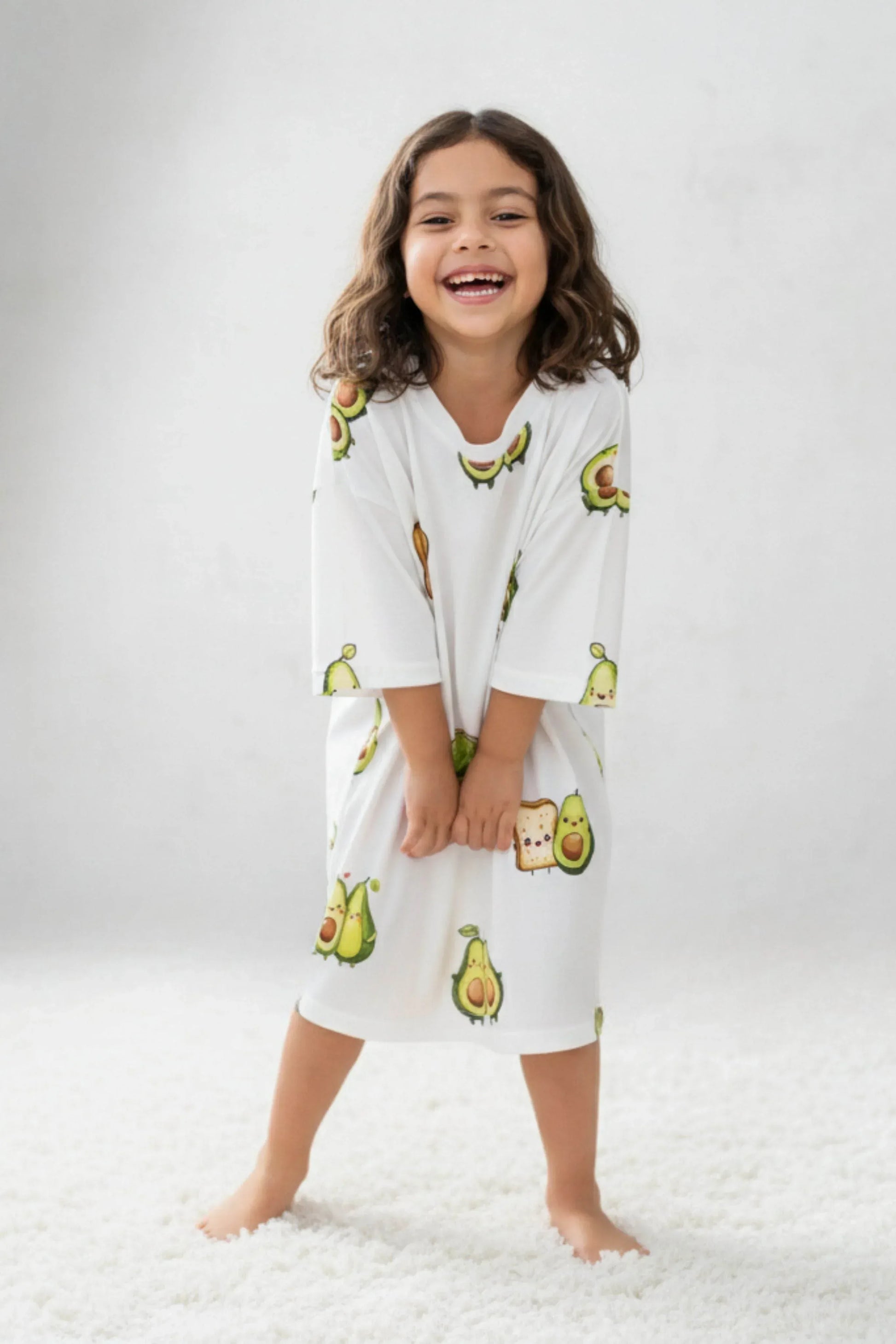 Child wearing a white oversized bamboo sleep Tee with avocado prints on a white background