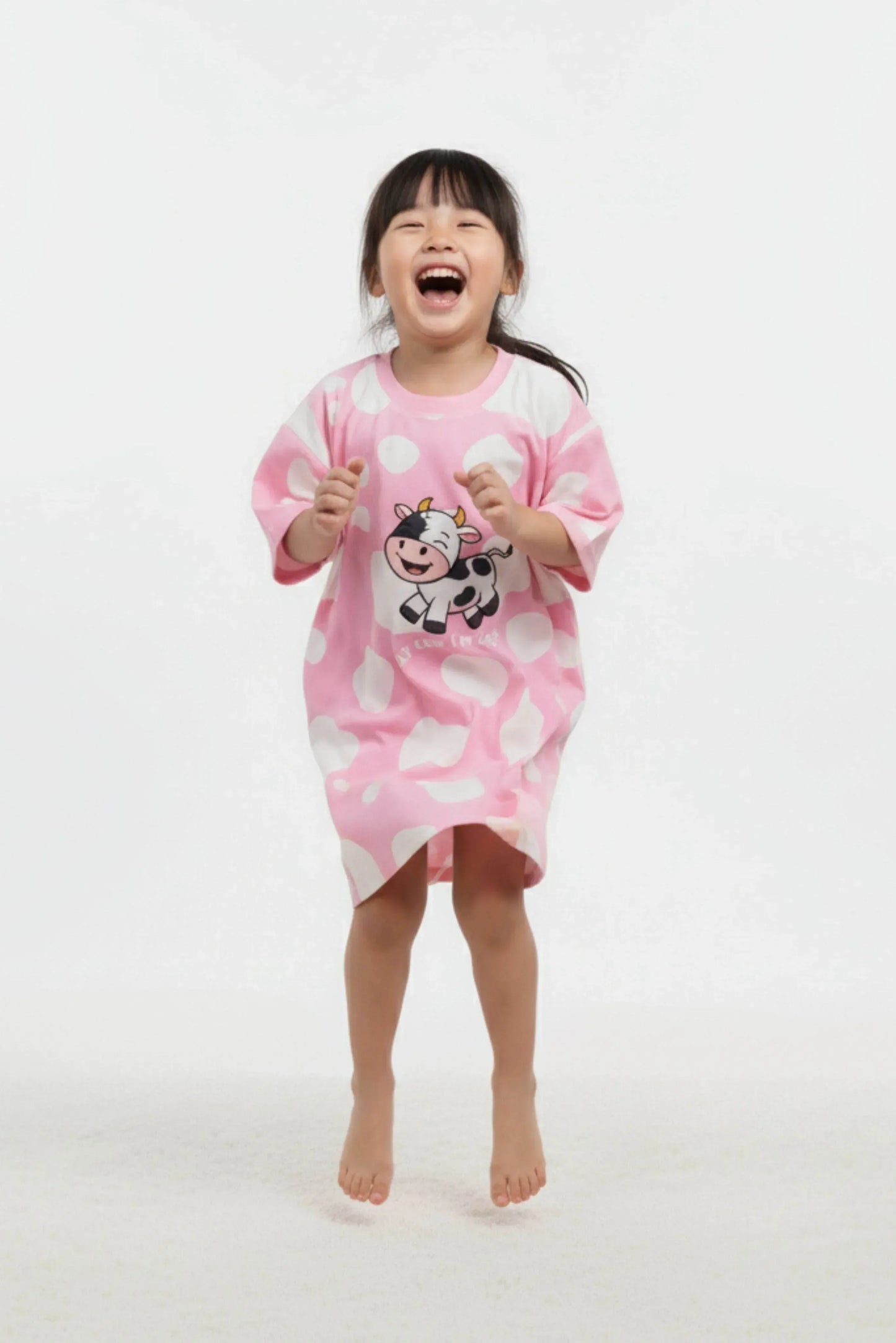Child wearing a pink oversized sleep tee with cow design on a white background