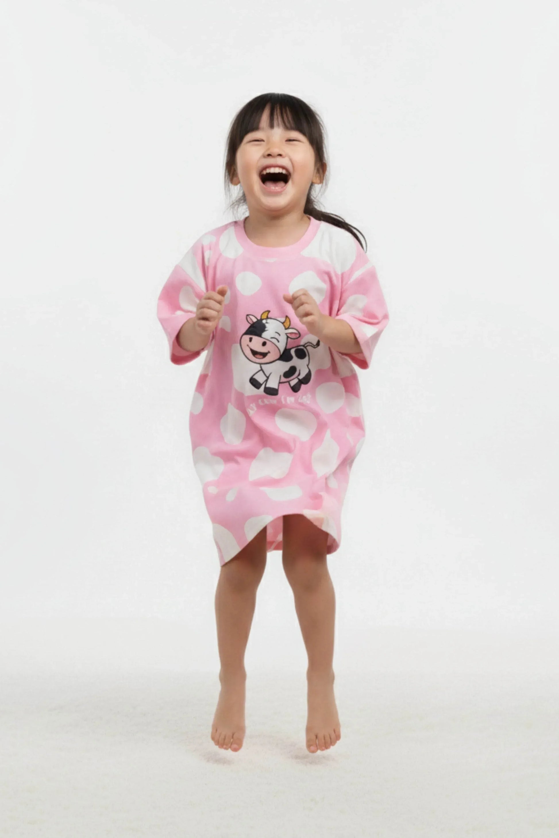 Child wearing a pink oversized sleep tee with cow design on a white background
