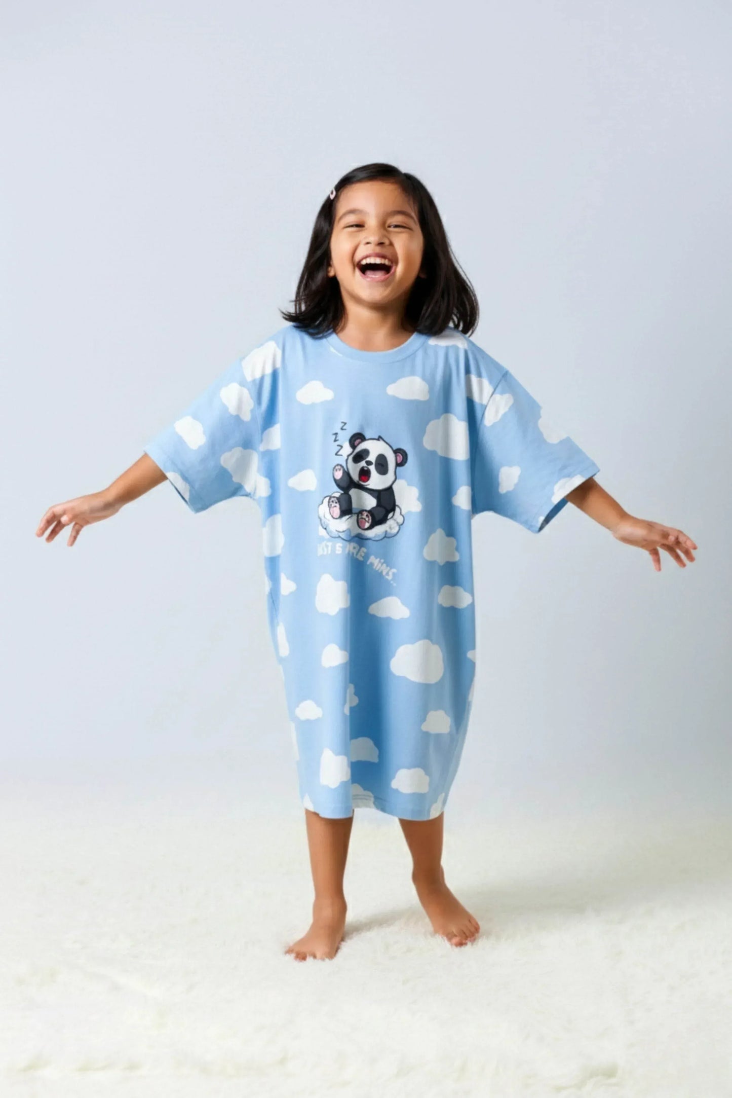 Child wearing blue oversized bamboo sleepwear with cloud and panda design on a white background