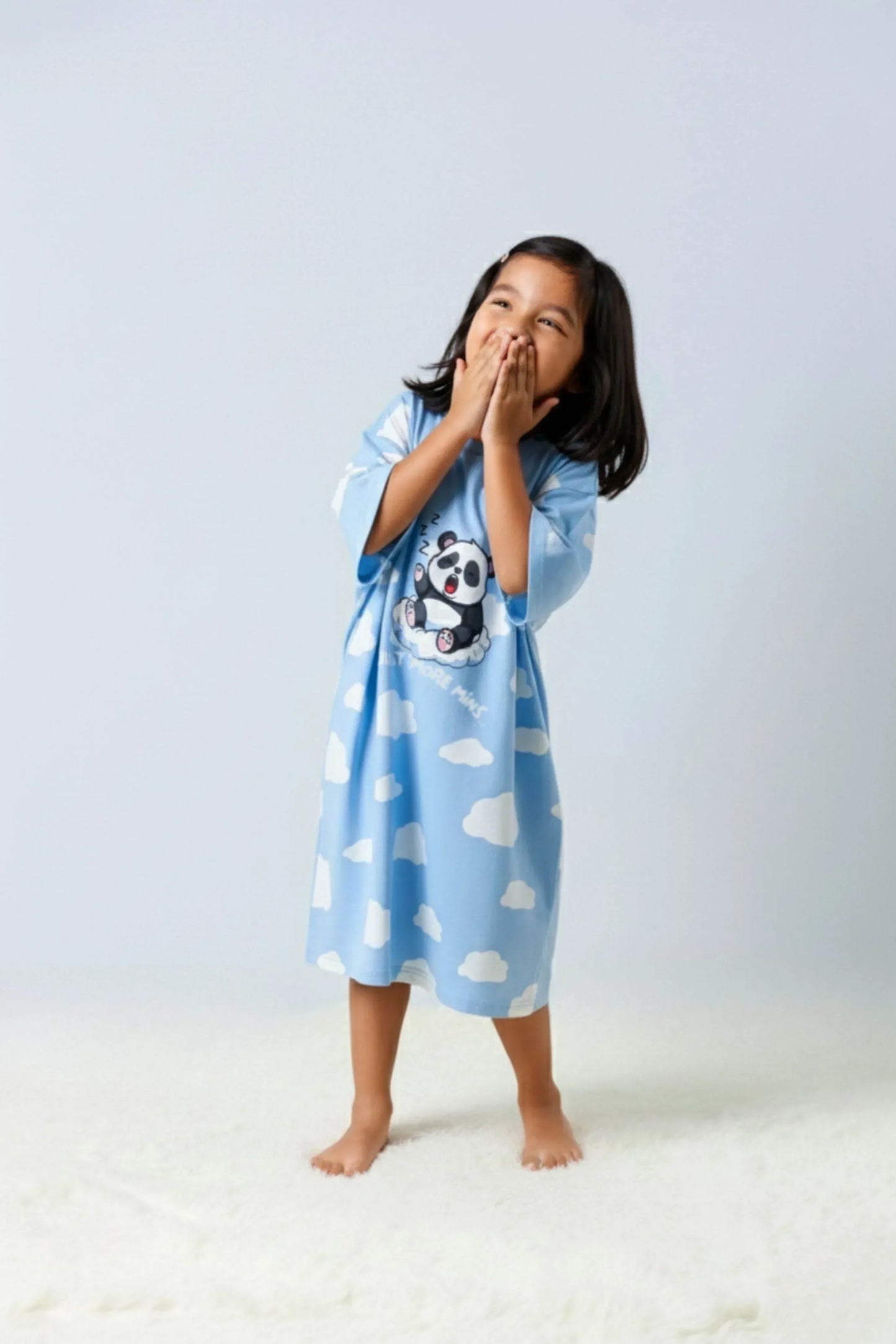 Happy young girl wearing an oversized bamboo sleep tee from MySleepTee Kids - Mini Me collection, featuring a cute sleeping panda print and cloud pattern – soft, breathable children's nightwear perfect for bedtime comfort