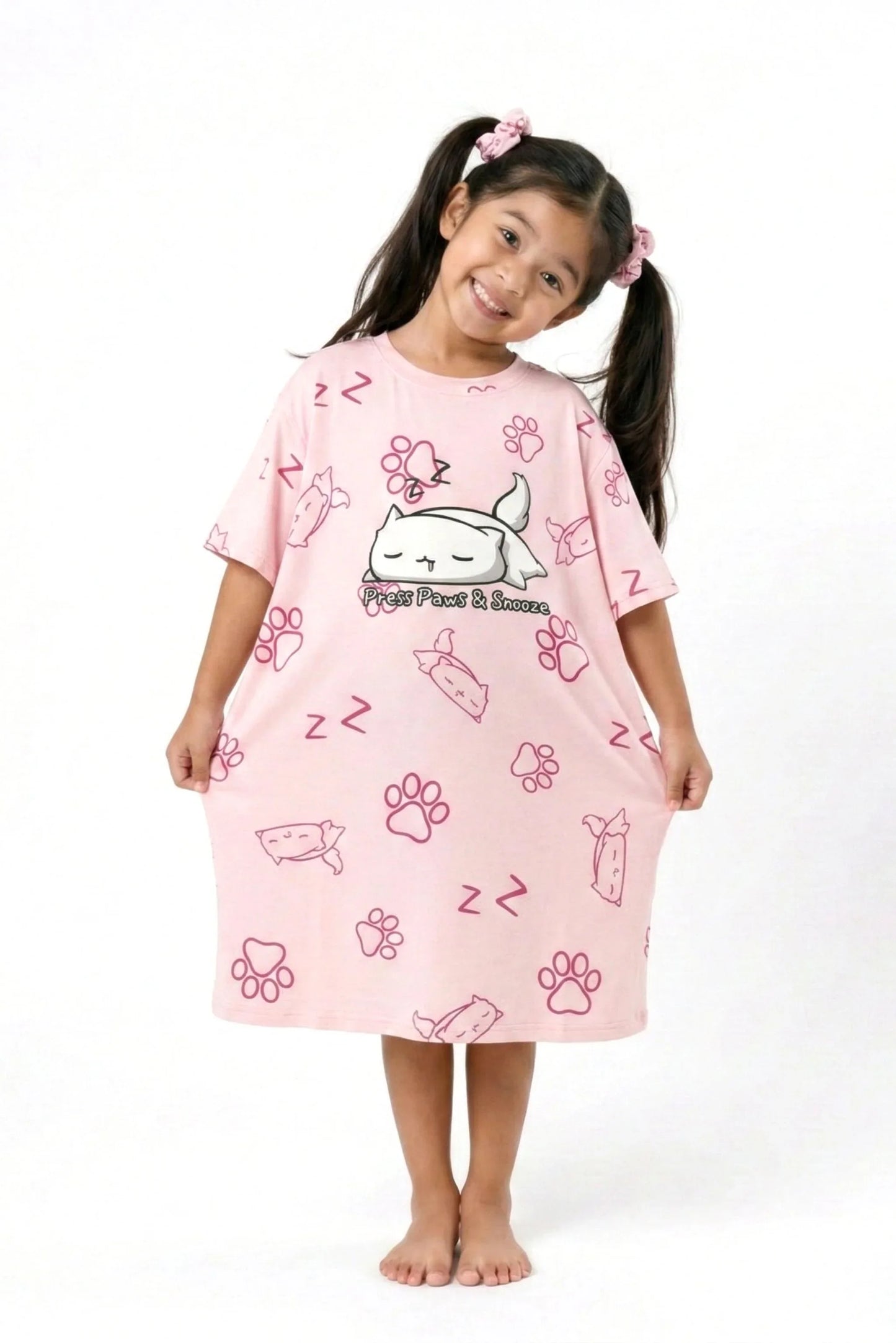 A young girl in pigtails smiling and holding the hem of her oversized MySleepTee pink bamboo sleep dress.