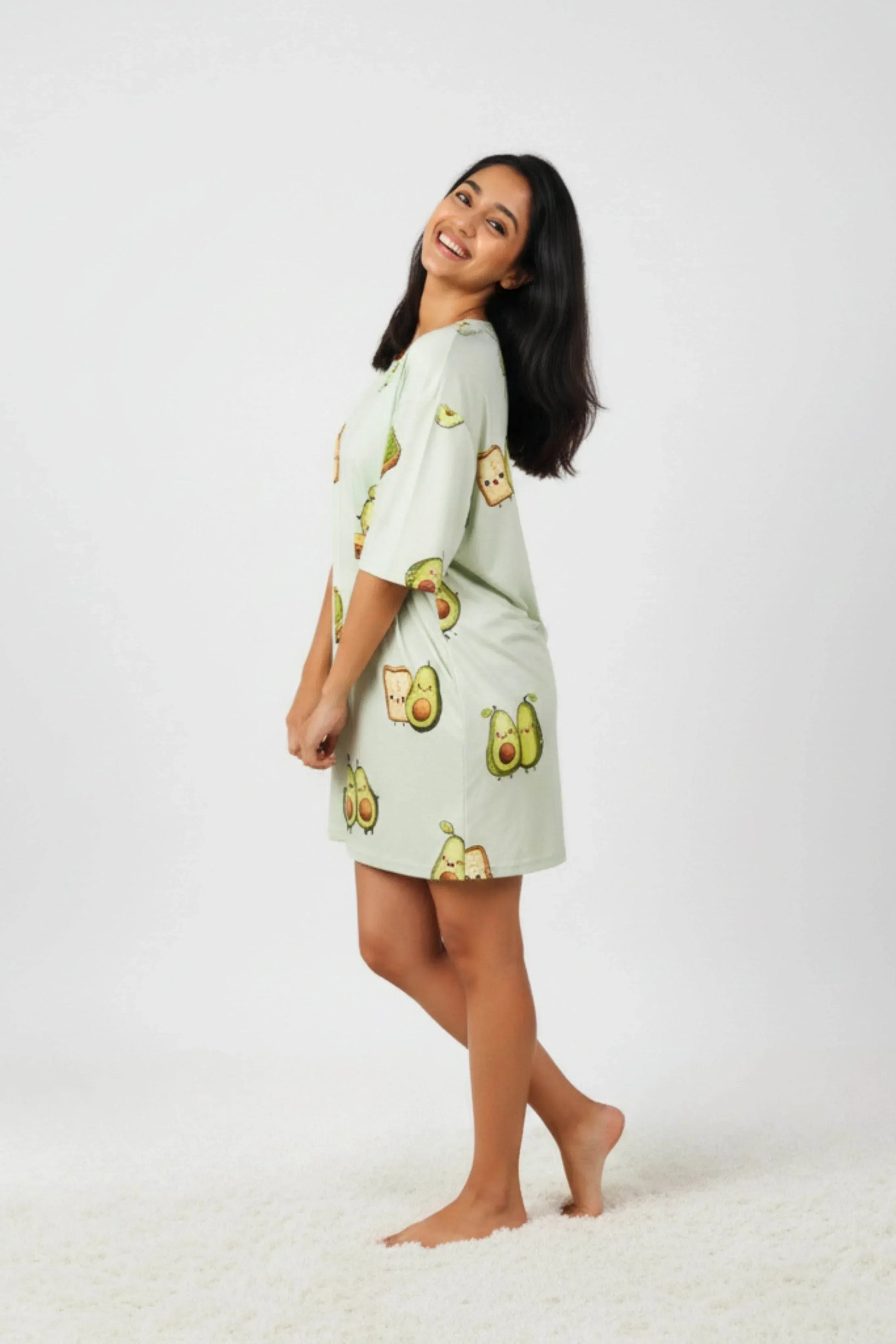 Woman wearing a light green oversized bamboo sleep tee from the petite collection from MySleepTee with  avocado kawaii illustrations on a white background