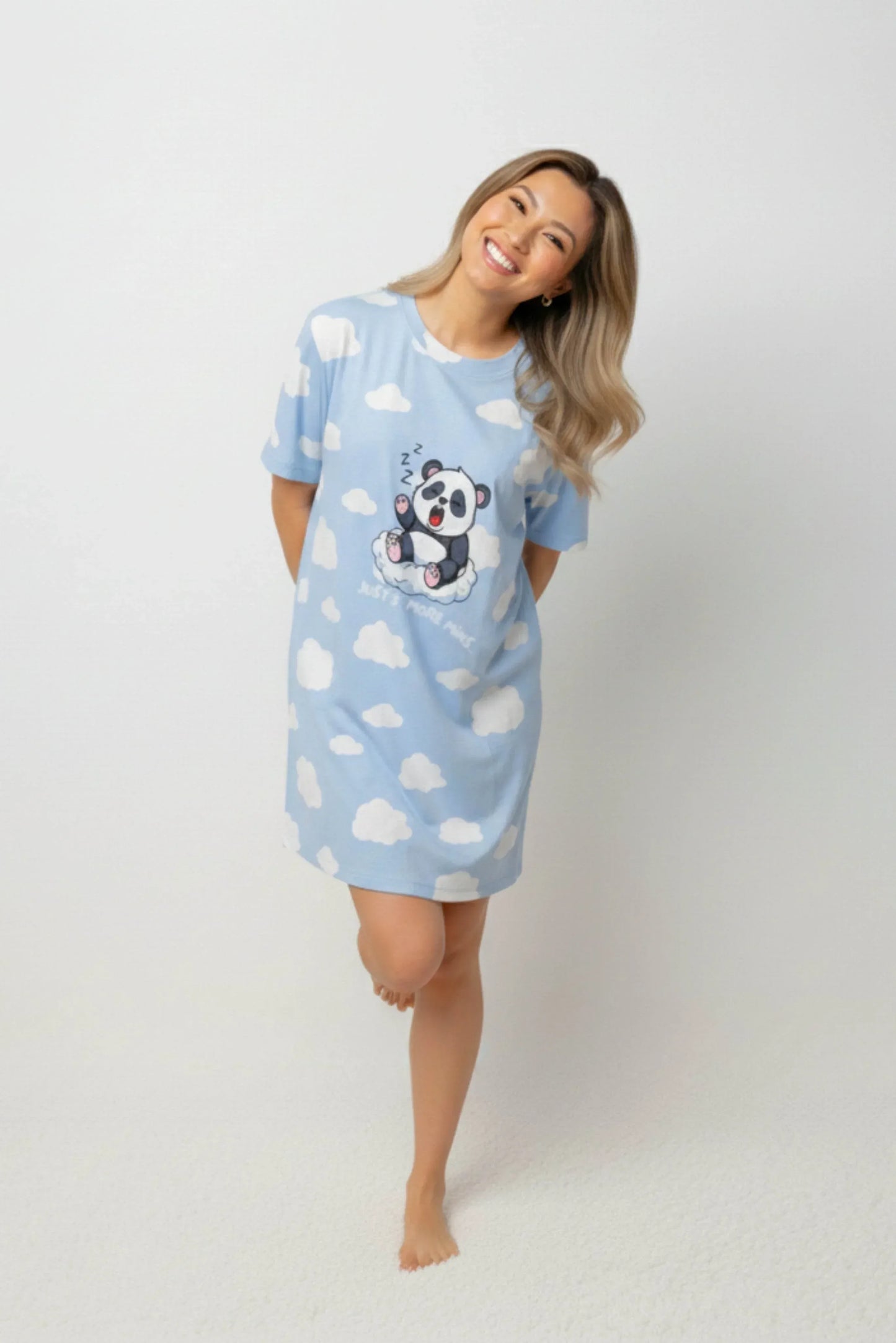 A woman smiling comfortably in a light blue oversized bamboo sleep tee from MySleepTee with a cute panda print.