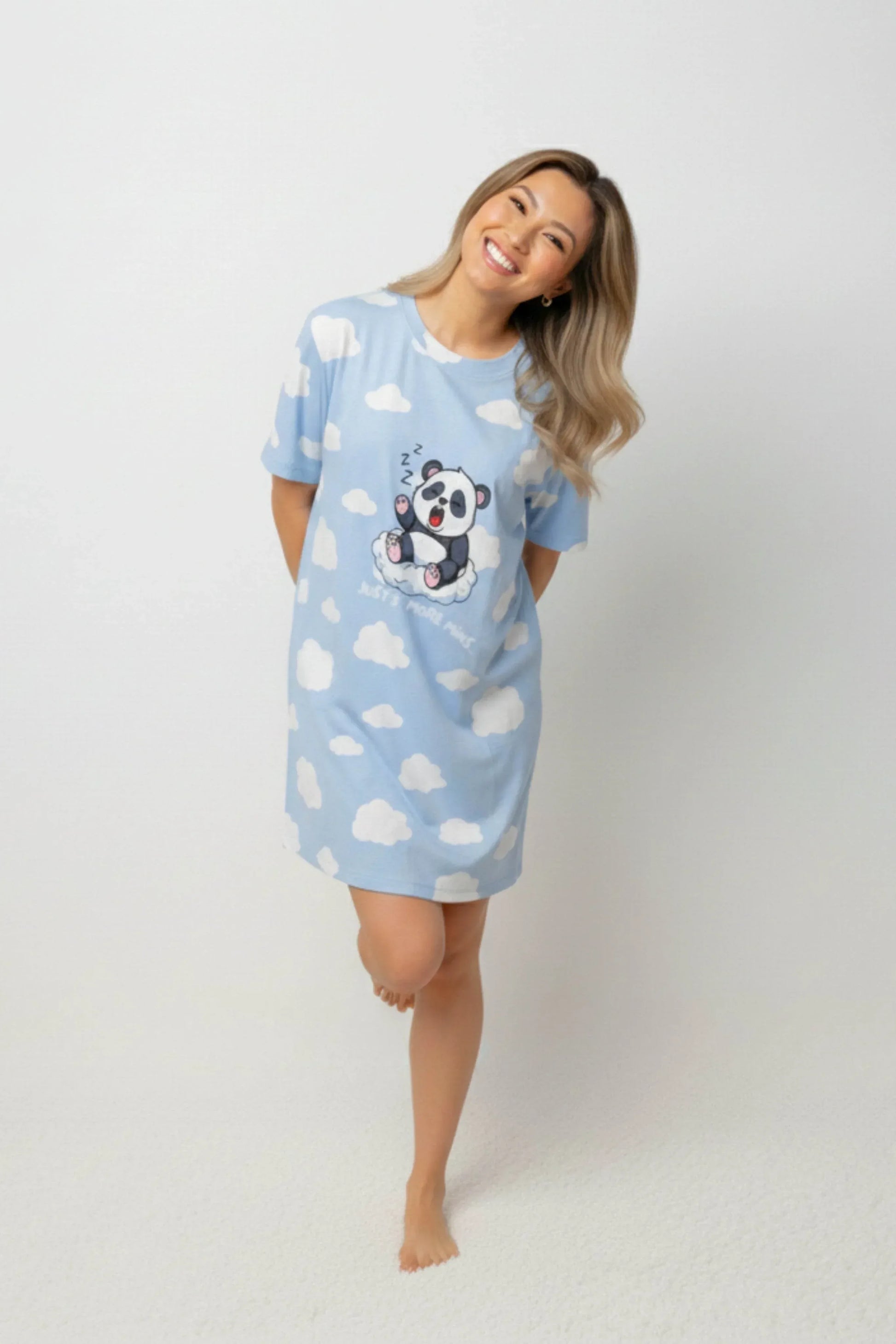 A woman smiling comfortably in a light blue oversized bamboo sleep tee from MySleepTee with a cute panda print.