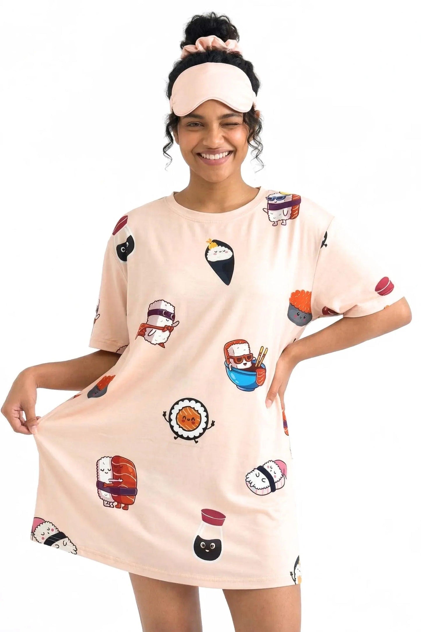 A smiling woman winking and stretching the hem of a light pink MySleepTee™ Soy Cozy Petite bamboo sleep dress featuring cute cartoon sushi characters. She is wearing a matching sleep mask pushed up on her head.