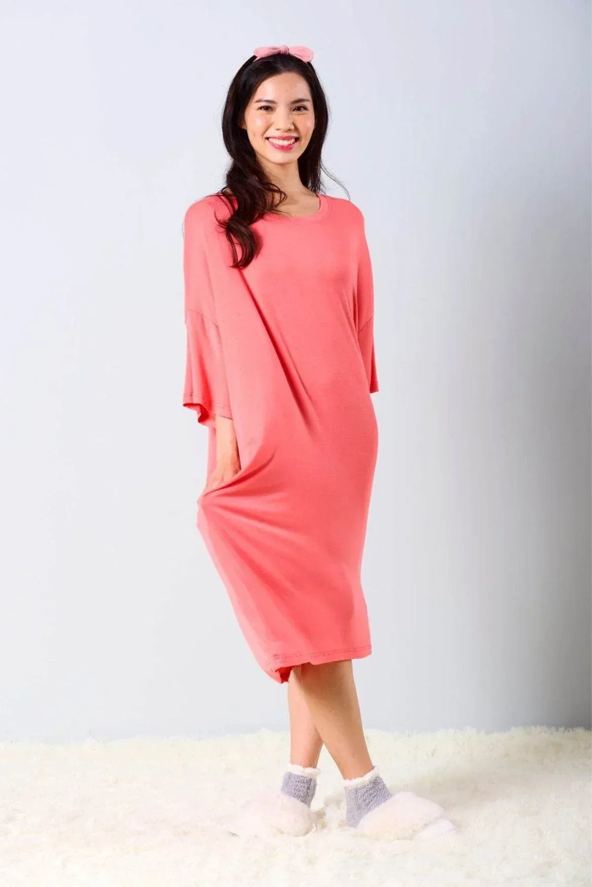 Woman wearing a rose colored sleep tee standing on a white surface with a light gray background