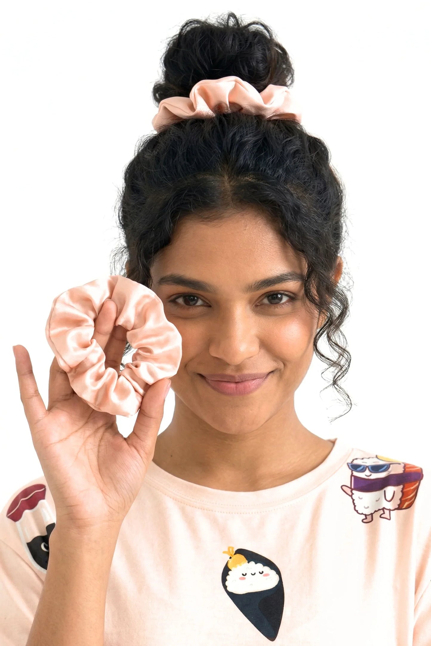 Woman holding salmon pink bamboo scrunchie with second scrunchie in bun wearing matching Soy Cozy sushi print sleep tee