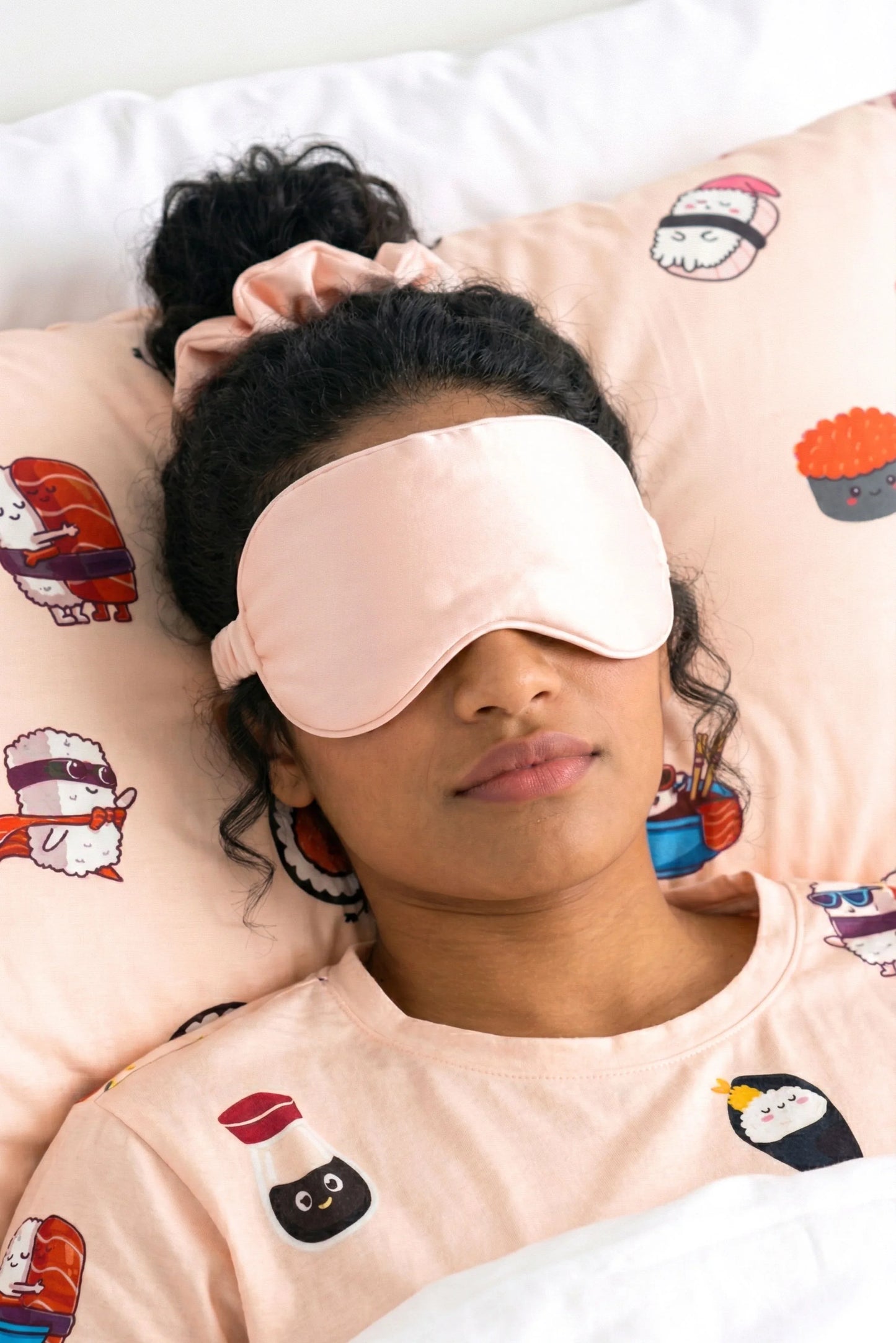 Woman sleeping with salmon pink bamboo scrunchie in hair wearing matching sleep mask on Soy Cozy sushi print pillow case