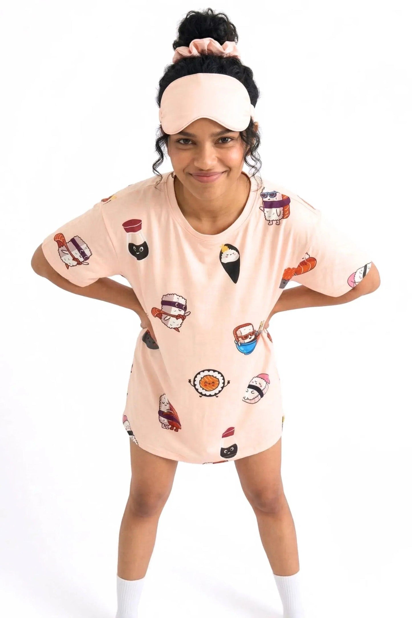 A playful woman leaning forward with her hands on her hips, wearing the lightweight MySleepTee™ Soy Cozy Petite bamboo sleep shirt with a cute sushi print and a matching sleep mask on her head.