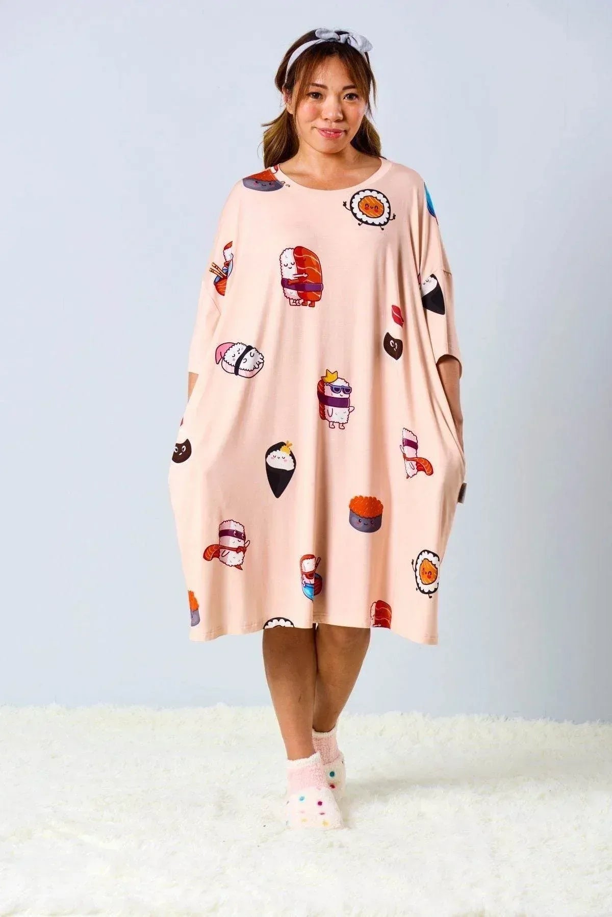 Woman wearing a salmon colored sleep tee with colorful sushi patterns against a light gray background