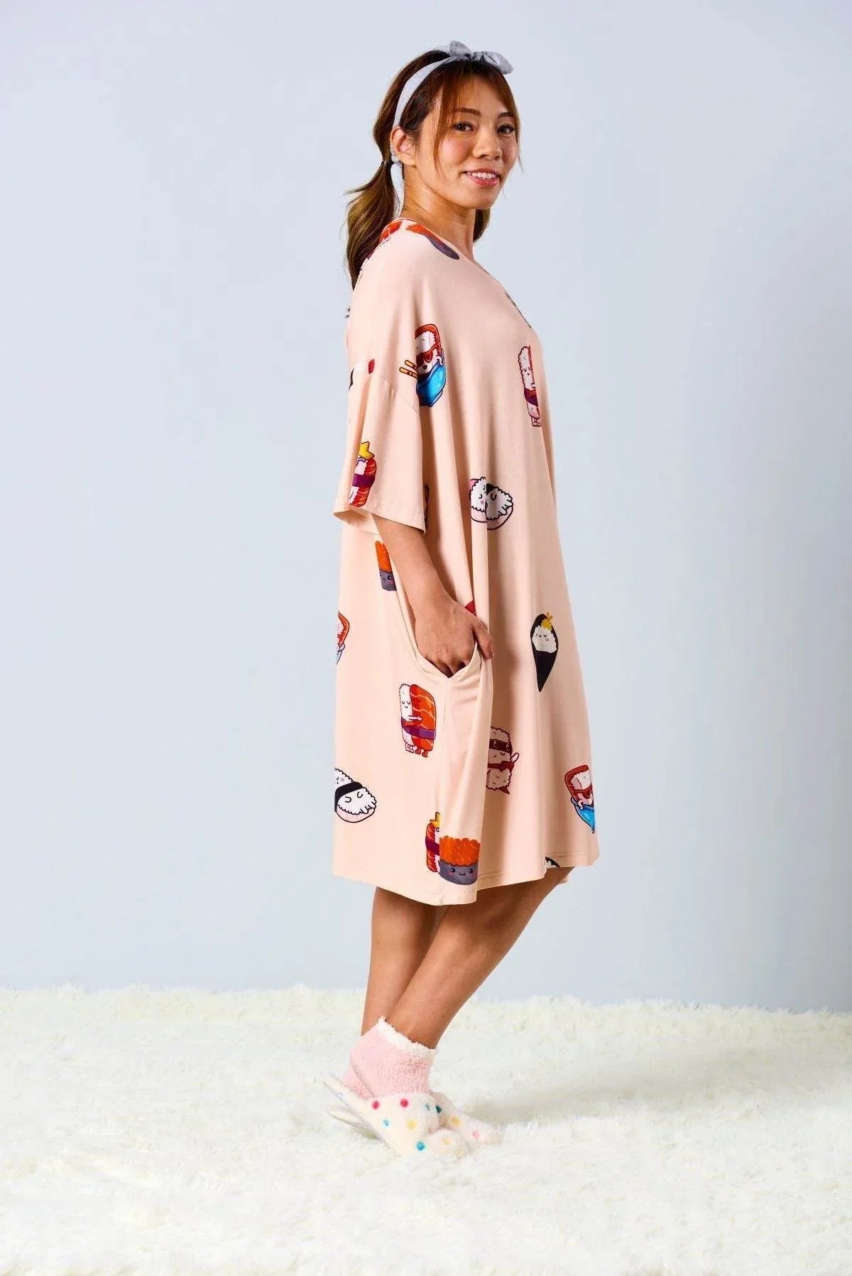Woman wearing a peach-colored sleep tee with colorful sushi designs on a light gray background
