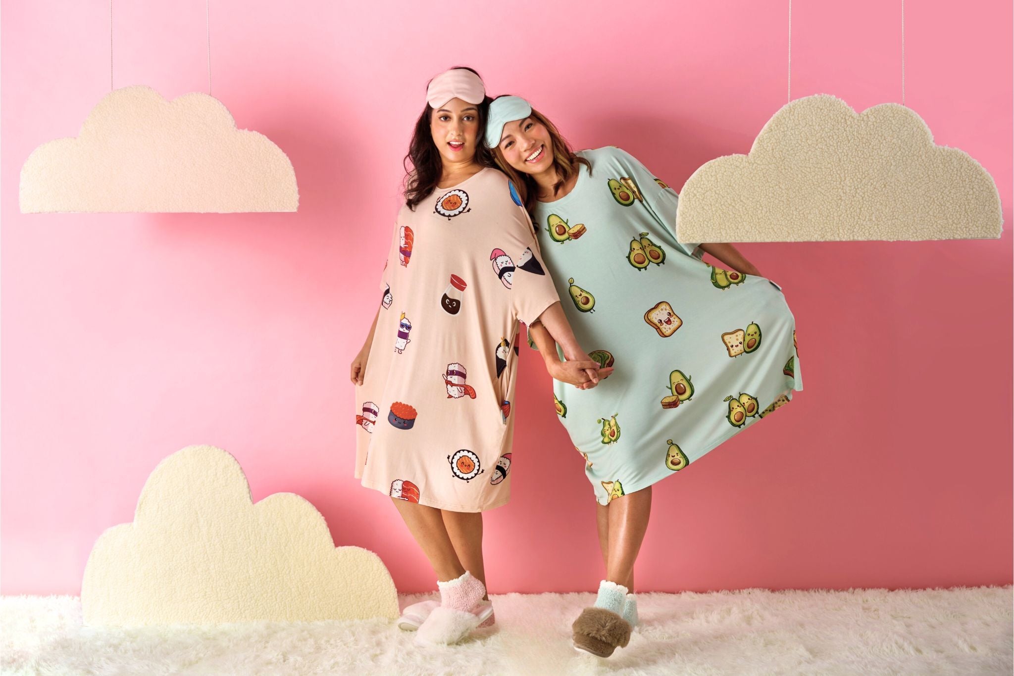 Two women wearing colorful sleep tees with cartoon designs against a pink wall.