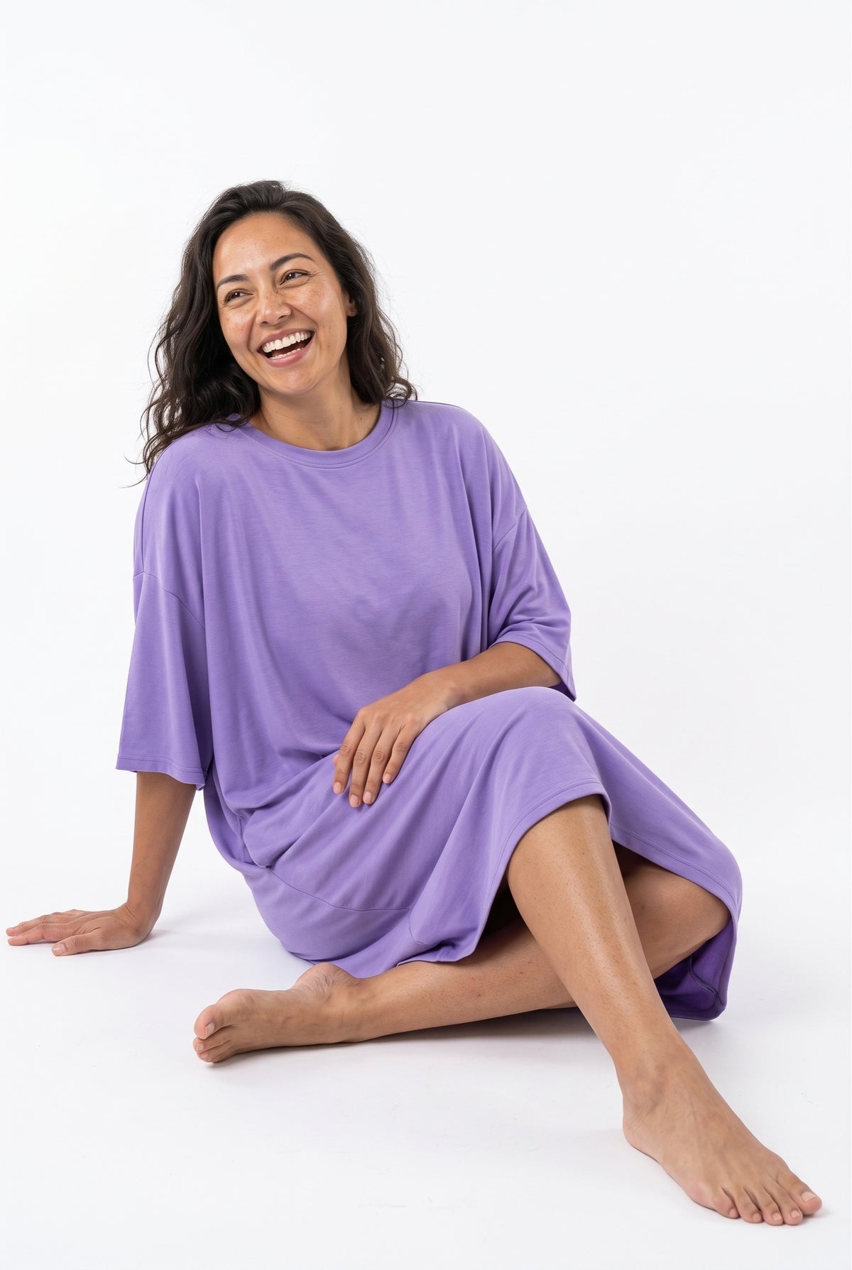 Woman laughing while lounging on the floor in a lilac purple bamboo oversized sleep tee, soft relaxed fit with wide dropped sleeves