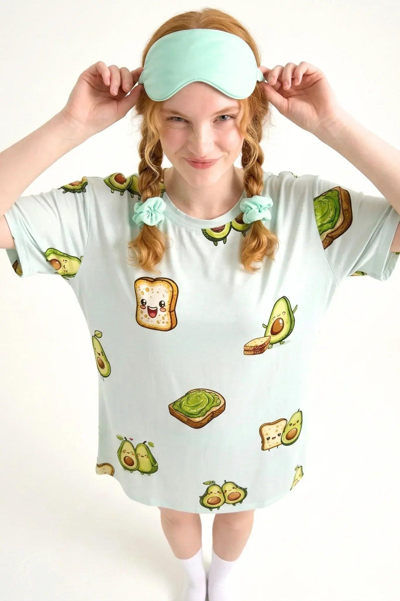 Top-down view of a woman playfully lifting her green sleep mask, wearing the ultra-soft, hypoallergenic Avo-Good Night bamboo sleep tee.