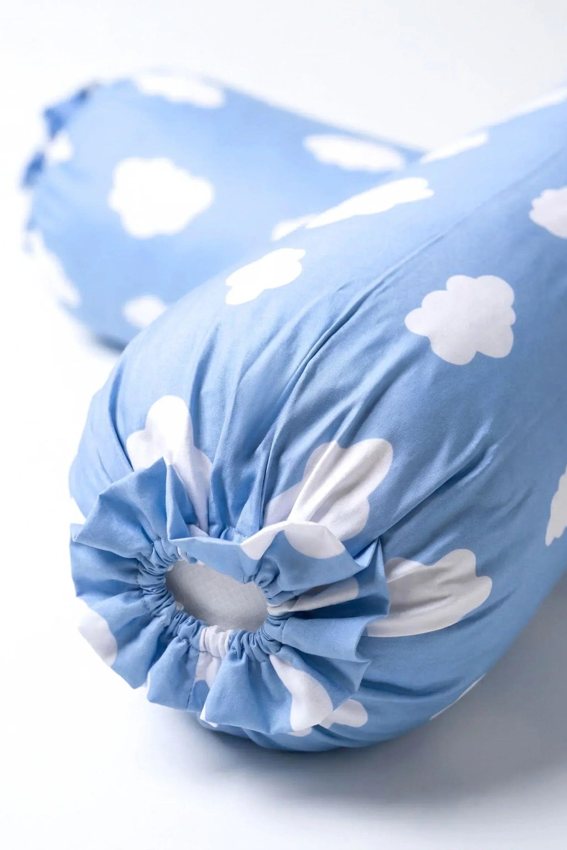 An artistic studio product shot focusing on the ends of two MySleepTee Un-bear-ably Sleepy bamboo bolster covers. The front cover, in sharp focus, displays the elasticated ruffled closure on the signature light blue cloud print fabric, with a second cover softly blurred in the background. Ultra-soft and cooling bamboo bedding.