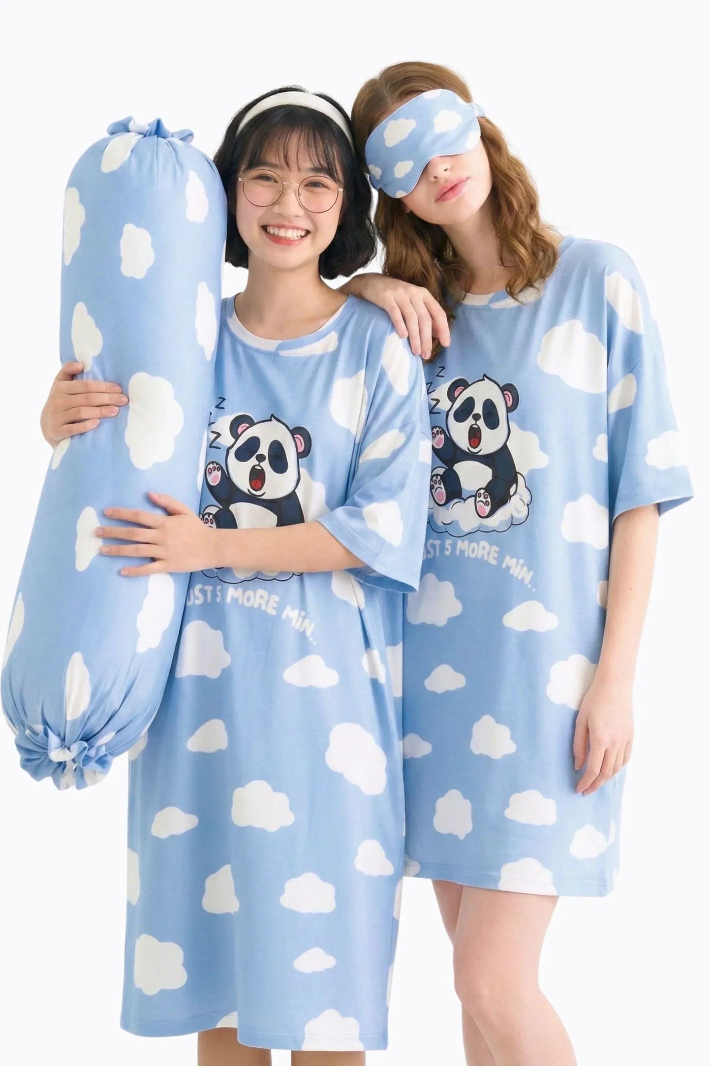 Two models in a studio setting showcasing the Un-bear-ably Sleepy collection by MySleepTee. One model holds the light blue, cloud-patterned bamboo bolster cover while wearing a matching panda oversized sleep tee. The second model wears a coordinating cloud sleep mask and panda shirt, demonstrating the complete cozy sleep set.