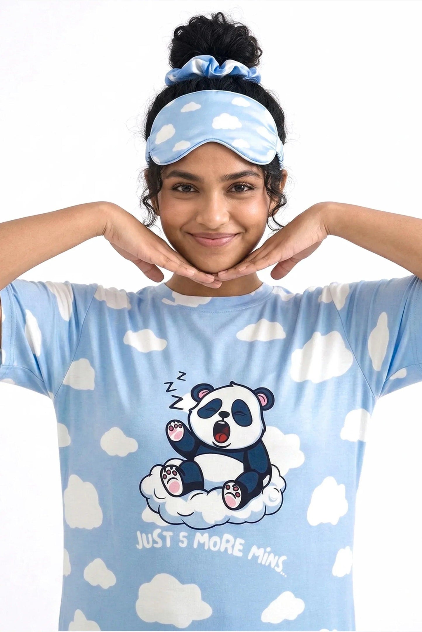 Close-up of a woman framing her smiling face, showcasing the Un-bear-ably Sleepy Petite light blue cloud pattern sleep tee from MySleepTee, wearing a matching sleep mask pushed up on her head.