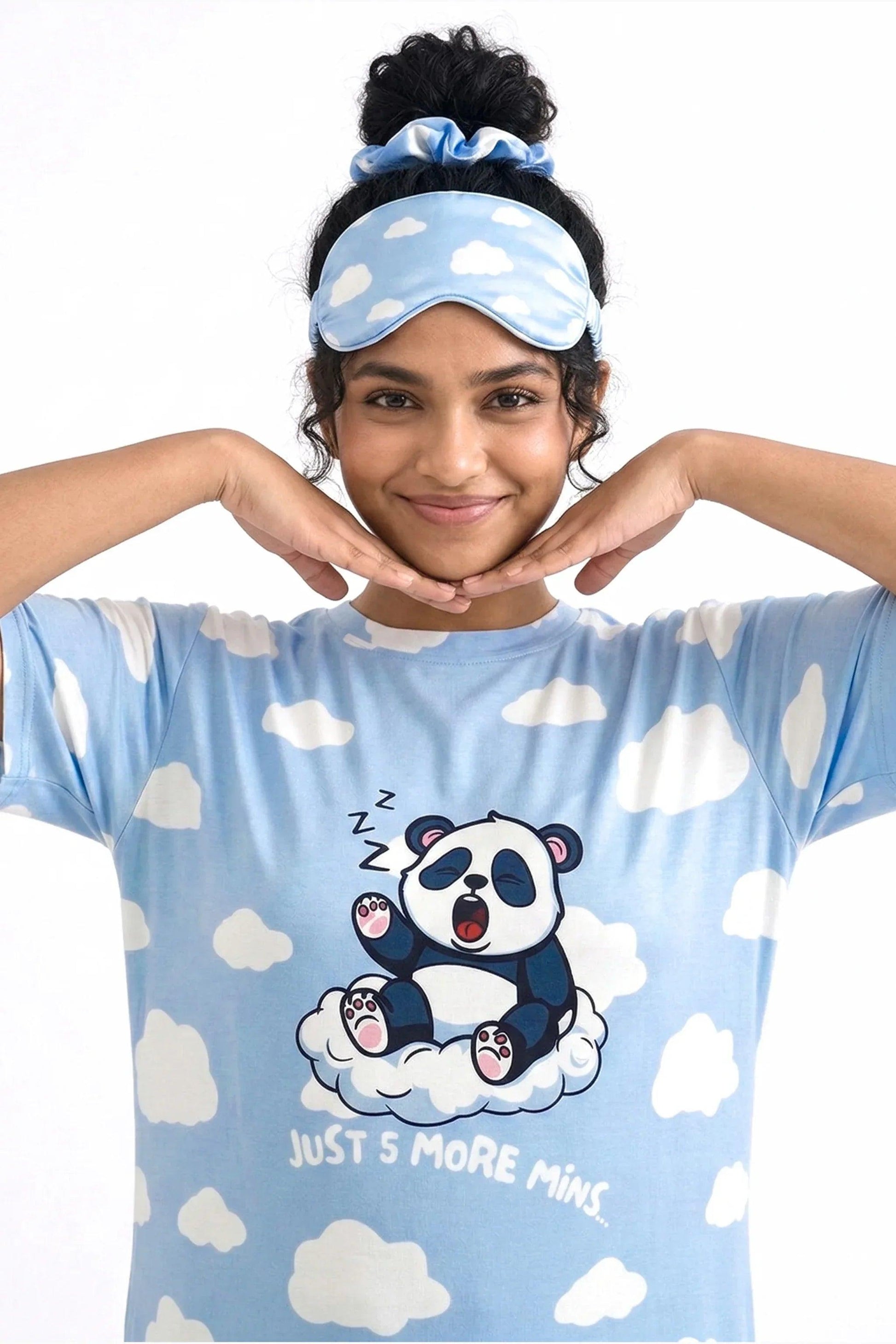 Close-up of a woman framing her smiling face, showcasing the Un-bear-ably Sleepy Petite light blue cloud pattern sleep tee from MySleepTee, wearing a matching sleep mask pushed up on her head.