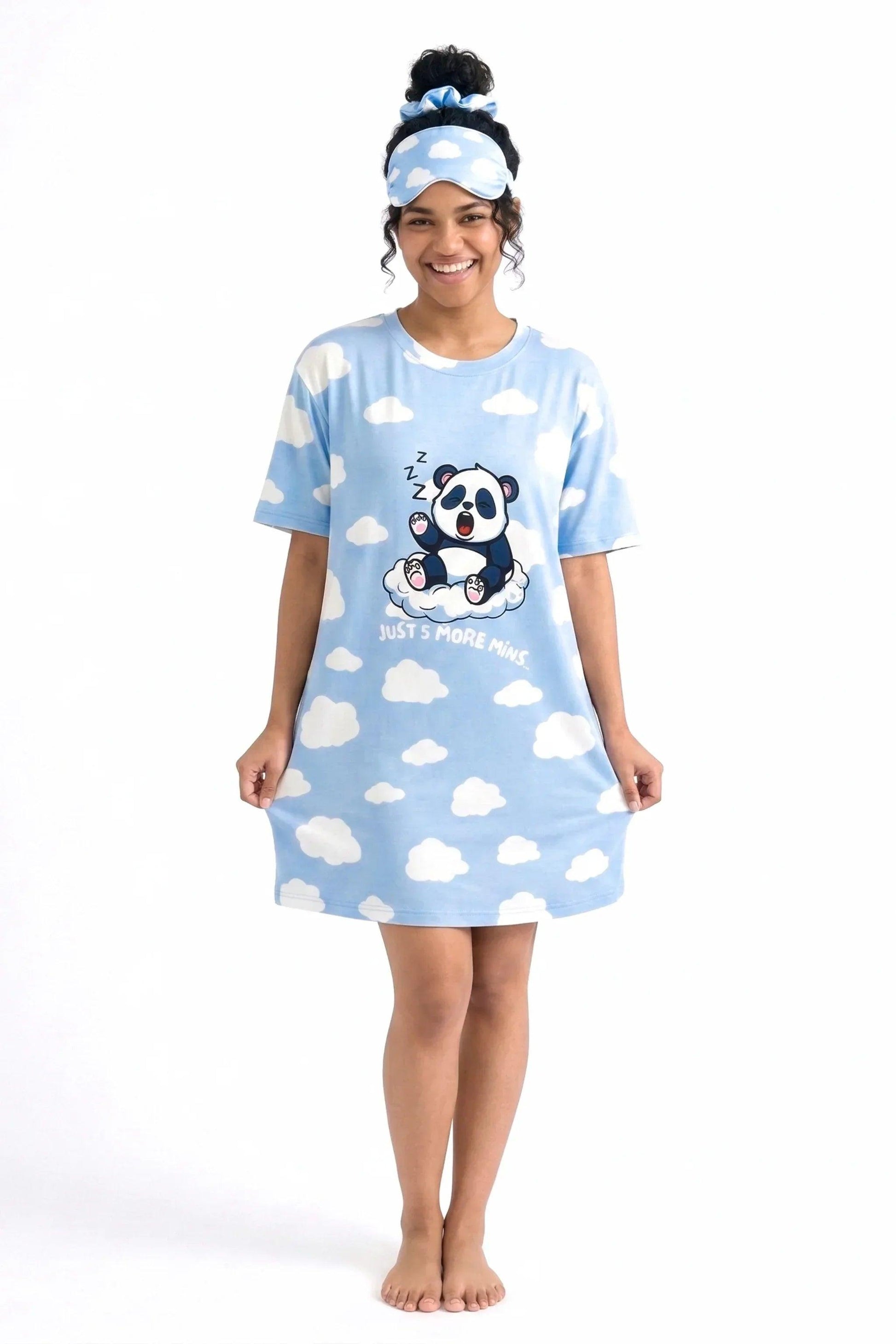 Full-length view of a smiling woman holding the hem of the Un-bear-ably Sleepy Petite nightshirt by MySleepTee, featuring white clouds, a yawning panda graphic, and a matching sleep mask.