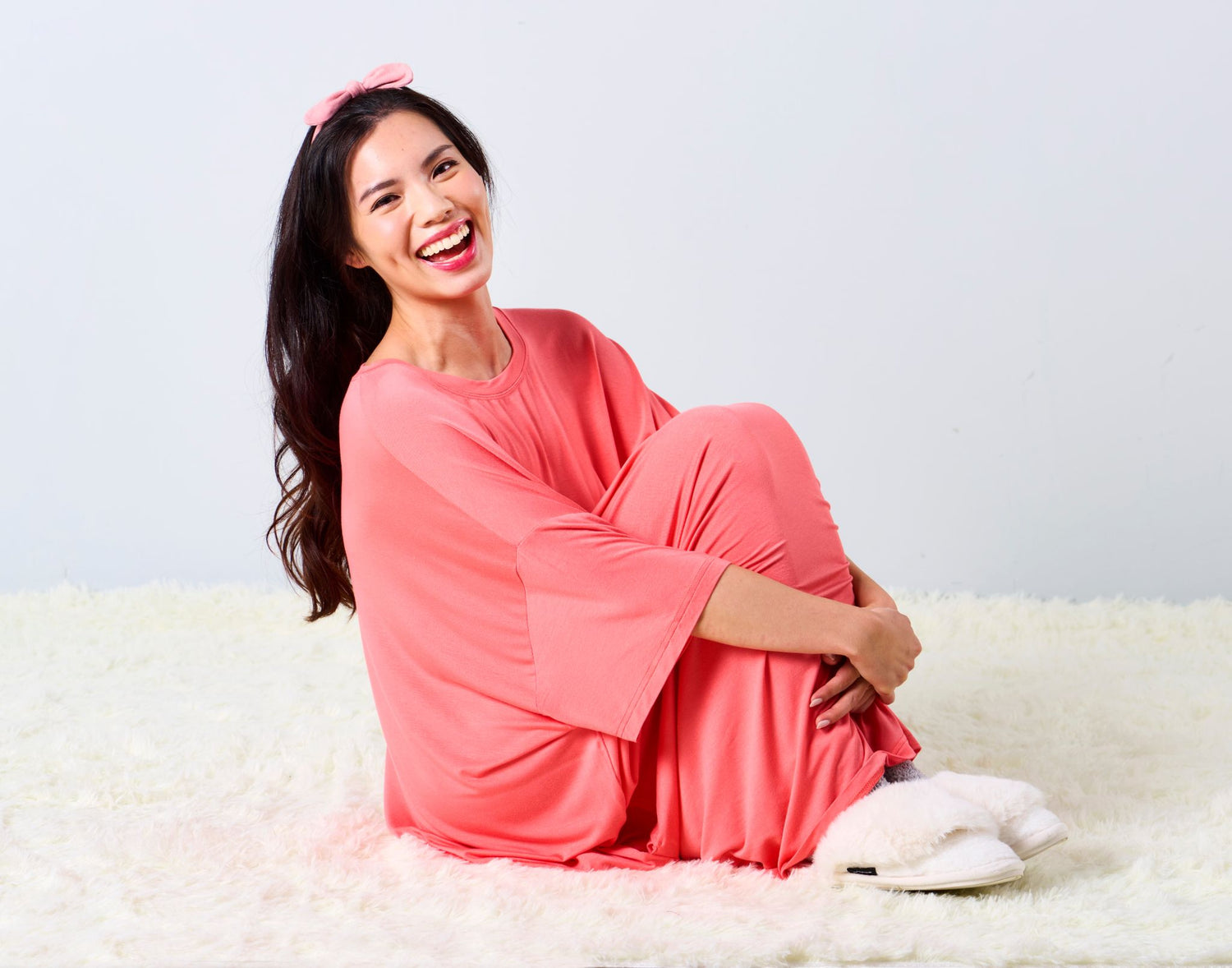 Woman in a red sleep tee by MySleepTee sitting on a white surface with a light gray background