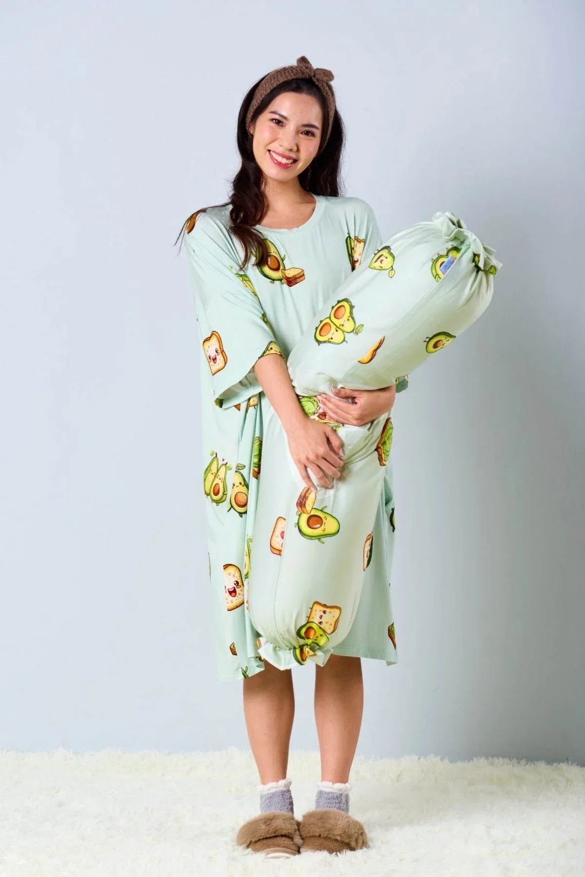 Woman wearing a light green night shirt with cartoon avocado print, holding a matching bolster 