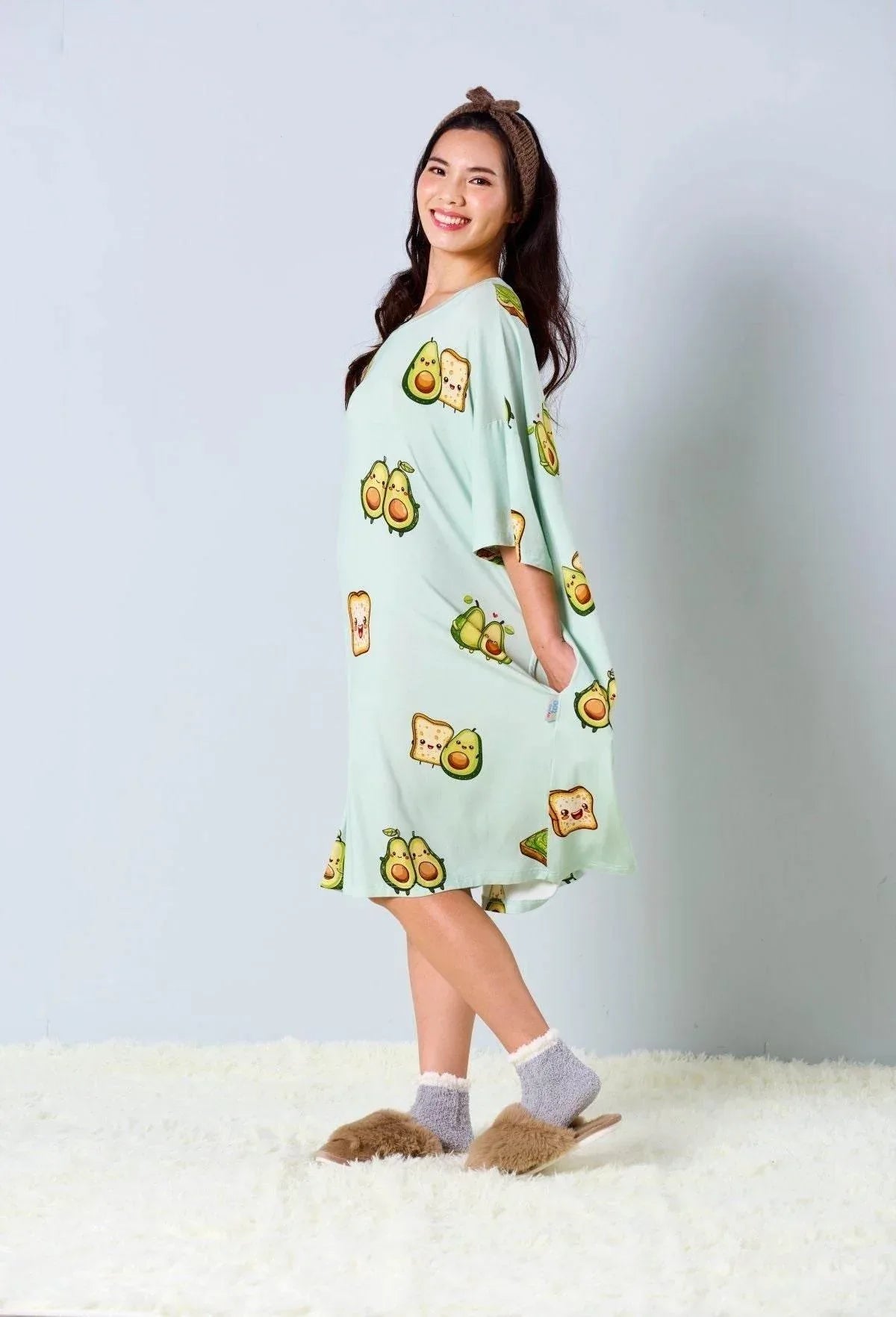 Woman wearing a light green dress with avocado print on a white background