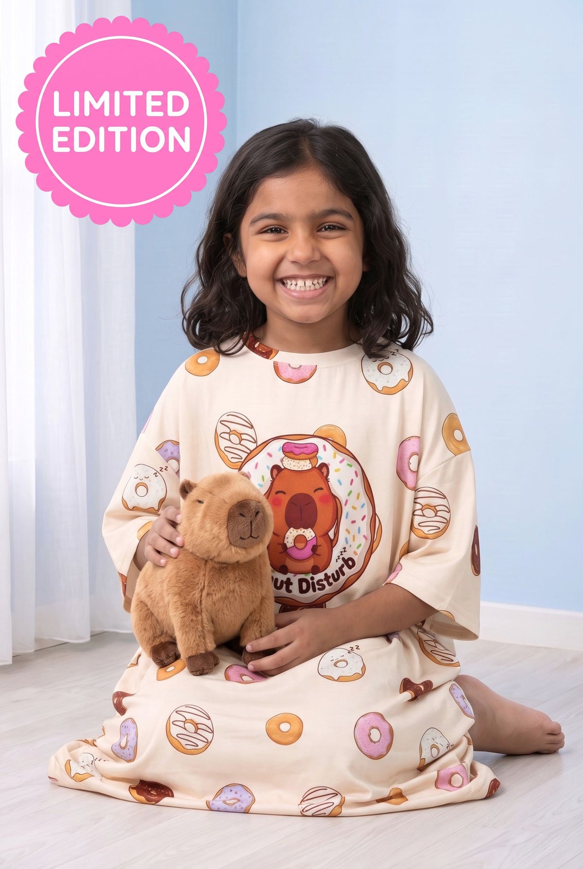 Young girl kneeling on the floor in the Donut Disturb Kids sleep tee, hugging a  capybara plush toy.